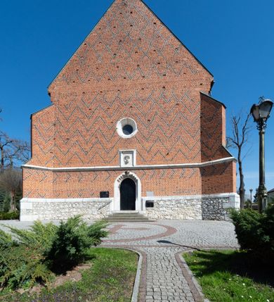 Zdjęcie nr 47: Kościół murowany z cegły, z użyciem zendrówki, na wysokim podmurowaniu z kamienia łupanego, jednonawowy, orientowany. 
Prezbiterium i nawa na planie prostokątów, nawa szersza i dłuższa od prezbiterium. Zakrystia na rzucie wydłużonego prostokąta przylega do wschodniej ściany prezbiterium, występując poza mury nawy. Prezbiterium od wschodu ujęte w narożach dwiema ukośnymi szkarpami, od południa jedną prostopadłą. Przy południowej ścianie nawy kruchta na planie kwadratu. Nawa w narożach ujęta szkarpami, od wschodu dwiema prostopadłymi, od zachodu ukośnymi. 
Prezbiterium dwuprzęsłowe, nakryte sklepieniem krzyżowo-żebrowym. Na zwornikach dwie tarcze z herbami Trzy Korony i Wieniawa. Zakrystia sklepiona kolebkowo. Nawa nakryta drewnianym stropem z kasetonami i rozetami. Kruchta sklepiona krzyżowo-żebrowo ze zwornikiem z tarczą z herbem Wieniawa. Otwór tęczowy w formie stojącego prostokąta zamkniętego łukiem ostrym. W zachodniej części nawy drewniany parapet chóru muzycznego wsparty na dwóch filarach. 
Fasada w jednej trzeciej wysokości odcięta kamiennym gzymsem kapnikowym, zakończona jodełkowym fryzem w partii muru, zwieńczona trójkątnym szczytem. Mur dekorowany zendrówką ułożoną „w zęby”, w partii szczytu w układzie rombowym. Na osi kamienny ostrołukowy portal o schodkowym nadprożu, dekorowanym krzyżującym się laskowaniem; węgary gładkie w jednej trzeciej wysokości przechodzące w piramidki i profilowanie powyżej. Nad portalem kamienna kwadratowa tablica, ujęta kamiennym obramieniem z tarczą z herbem Wieniawa. Ponad nią, na osi okulus w kamiennym obramieniu. 
Elewacje północna i południowa w części nawy w jednej trzeciej wysokości przedzielone kamiennym gzymsem kapnikowym, na zakończeniu ścian z gzymsem wieńczącym. Mur dekorowany zendrówką w układzie rombowym. Na elewacji południowej cztery okna w formie wydłużonego, stojącego prostokąta zamkniętego łukiem ostrym, w kamiennych obramieniach, podzielone laskowaniem. Południowa ściana prezbiterium zakończona gzymsem wieńczącym, w górnej części muru dekorowana zendrówką ułożoną „w zęby”. 
Szkarpy opinające nawę uskokowe, zwężające się ku górze, nakryte daszkami pulpitowymi. Szkarpy opinające prezbiterium nakryte daszkami pulpitowymi, podzielone gzymsami kapnikowymi. 
Kruchta od strony wschodniej i zachodniej podzielona kamiennym gzymsem kapnikowym, od południa zakończona gzymsem wieńczącym. Na ścianie południowej kruchty kamienny, ostrołukowy portal, o schodkowym nadprożu, dekorowanym krzyżującym się laskowaniem; węgary gładkie, w jednej trzeciej wysokości przechodzące w piramidki i profilowanie powyżej. Nad portalem kamienna tarcza z herbem Wieniawa. 
Elewacja wschodnia zwieńczona trójkątnym szczytem, w którego partii mur dekorowany jest zendrówką w układzie rombowym. Na osi okno w formie wydłużonego, stojącego prostokąta zamkniętego łukiem ostrym, w kamiennym obramieniu, zamurowane w trzech piątych wysokości, zakończone daszkiem pulpitowym. W dolnej części okna znajduje się ogrójec. 
Nawa i prezbiterium nakryte osobnymi blaszanymi dachami dwuspadowymi, kruchta i zakrystia pulpitowymi. Nad nawą blaszana wieżyczka na sygnaturkę z latarnią i hełmem baniastym.





