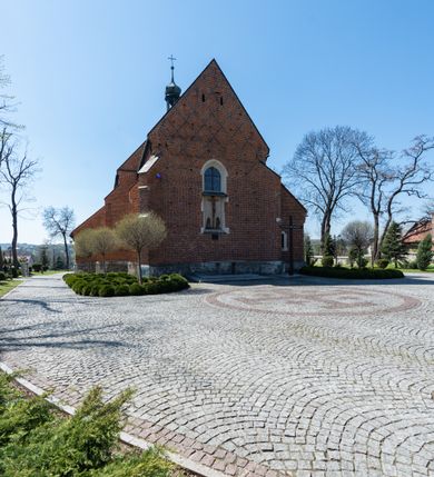 Zdjęcie nr 31: Kościół murowany z cegły, z użyciem zendrówki, na wysokim podmurowaniu z kamienia łupanego, jednonawowy, orientowany. 
Prezbiterium i nawa na planie prostokątów, nawa szersza i dłuższa od prezbiterium. Zakrystia na rzucie wydłużonego prostokąta przylega do wschodniej ściany prezbiterium, występując poza mury nawy. Prezbiterium od wschodu ujęte w narożach dwiema ukośnymi szkarpami, od południa jedną prostopadłą. Przy południowej ścianie nawy kruchta na planie kwadratu. Nawa w narożach ujęta szkarpami, od wschodu dwiema prostopadłymi, od zachodu ukośnymi. 
Prezbiterium dwuprzęsłowe, nakryte sklepieniem krzyżowo-żebrowym. Na zwornikach dwie tarcze z herbami Trzy Korony i Wieniawa. Zakrystia sklepiona kolebkowo. Nawa nakryta drewnianym stropem z kasetonami i rozetami. Kruchta sklepiona krzyżowo-żebrowo ze zwornikiem z tarczą z herbem Wieniawa. Otwór tęczowy w formie stojącego prostokąta zamkniętego łukiem ostrym. W zachodniej części nawy drewniany parapet chóru muzycznego wsparty na dwóch filarach. 
Fasada w jednej trzeciej wysokości odcięta kamiennym gzymsem kapnikowym, zakończona jodełkowym fryzem w partii muru, zwieńczona trójkątnym szczytem. Mur dekorowany zendrówką ułożoną „w zęby”, w partii szczytu w układzie rombowym. Na osi kamienny ostrołukowy portal o schodkowym nadprożu, dekorowanym krzyżującym się laskowaniem; węgary gładkie w jednej trzeciej wysokości przechodzące w piramidki i profilowanie powyżej. Nad portalem kamienna kwadratowa tablica, ujęta kamiennym obramieniem z tarczą z herbem Wieniawa. Ponad nią, na osi okulus w kamiennym obramieniu. 
Elewacje północna i południowa w części nawy w jednej trzeciej wysokości przedzielone kamiennym gzymsem kapnikowym, na zakończeniu ścian z gzymsem wieńczącym. Mur dekorowany zendrówką w układzie rombowym. Na elewacji południowej cztery okna w formie wydłużonego, stojącego prostokąta zamkniętego łukiem ostrym, w kamiennych obramieniach, podzielone laskowaniem. Południowa ściana prezbiterium zakończona gzymsem wieńczącym, w górnej części muru dekorowana zendrówką ułożoną „w zęby”. 
Szkarpy opinające nawę uskokowe, zwężające się ku górze, nakryte daszkami pulpitowymi. Szkarpy opinające prezbiterium nakryte daszkami pulpitowymi, podzielone gzymsami kapnikowymi. 
Kruchta od strony wschodniej i zachodniej podzielona kamiennym gzymsem kapnikowym, od południa zakończona gzymsem wieńczącym. Na ścianie południowej kruchty kamienny, ostrołukowy portal, o schodkowym nadprożu, dekorowanym krzyżującym się laskowaniem; węgary gładkie, w jednej trzeciej wysokości przechodzące w piramidki i profilowanie powyżej. Nad portalem kamienna tarcza z herbem Wieniawa. 
Elewacja wschodnia zwieńczona trójkątnym szczytem, w którego partii mur dekorowany jest zendrówką w układzie rombowym. Na osi okno w formie wydłużonego, stojącego prostokąta zamkniętego łukiem ostrym, w kamiennym obramieniu, zamurowane w trzech piątych wysokości, zakończone daszkiem pulpitowym. W dolnej części okna znajduje się ogrójec. 
Nawa i prezbiterium nakryte osobnymi blaszanymi dachami dwuspadowymi, kruchta i zakrystia pulpitowymi. Nad nawą blaszana wieżyczka na sygnaturkę z latarnią i hełmem baniastym.





