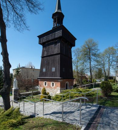 Zdjęcie nr 49: Kościół murowany z cegły, z użyciem zendrówki, na wysokim podmurowaniu z kamienia łupanego, jednonawowy, orientowany. 
Prezbiterium i nawa na planie prostokątów, nawa szersza i dłuższa od prezbiterium. Zakrystia na rzucie wydłużonego prostokąta przylega do wschodniej ściany prezbiterium, występując poza mury nawy. Prezbiterium od wschodu ujęte w narożach dwiema ukośnymi szkarpami, od południa jedną prostopadłą. Przy południowej ścianie nawy kruchta na planie kwadratu. Nawa w narożach ujęta szkarpami, od wschodu dwiema prostopadłymi, od zachodu ukośnymi. 
Prezbiterium dwuprzęsłowe, nakryte sklepieniem krzyżowo-żebrowym. Na zwornikach dwie tarcze z herbami Trzy Korony i Wieniawa. Zakrystia sklepiona kolebkowo. Nawa nakryta drewnianym stropem z kasetonami i rozetami. Kruchta sklepiona krzyżowo-żebrowo ze zwornikiem z tarczą z herbem Wieniawa. Otwór tęczowy w formie stojącego prostokąta zamkniętego łukiem ostrym. W zachodniej części nawy drewniany parapet chóru muzycznego wsparty na dwóch filarach. 
Fasada w jednej trzeciej wysokości odcięta kamiennym gzymsem kapnikowym, zakończona jodełkowym fryzem w partii muru, zwieńczona trójkątnym szczytem. Mur dekorowany zendrówką ułożoną „w zęby”, w partii szczytu w układzie rombowym. Na osi kamienny ostrołukowy portal o schodkowym nadprożu, dekorowanym krzyżującym się laskowaniem; węgary gładkie w jednej trzeciej wysokości przechodzące w piramidki i profilowanie powyżej. Nad portalem kamienna kwadratowa tablica, ujęta kamiennym obramieniem z tarczą z herbem Wieniawa. Ponad nią, na osi okulus w kamiennym obramieniu. 
Elewacje północna i południowa w części nawy w jednej trzeciej wysokości przedzielone kamiennym gzymsem kapnikowym, na zakończeniu ścian z gzymsem wieńczącym. Mur dekorowany zendrówką w układzie rombowym. Na elewacji południowej cztery okna w formie wydłużonego, stojącego prostokąta zamkniętego łukiem ostrym, w kamiennych obramieniach, podzielone laskowaniem. Południowa ściana prezbiterium zakończona gzymsem wieńczącym, w górnej części muru dekorowana zendrówką ułożoną „w zęby”. 
Szkarpy opinające nawę uskokowe, zwężające się ku górze, nakryte daszkami pulpitowymi. Szkarpy opinające prezbiterium nakryte daszkami pulpitowymi, podzielone gzymsami kapnikowymi. 
Kruchta od strony wschodniej i zachodniej podzielona kamiennym gzymsem kapnikowym, od południa zakończona gzymsem wieńczącym. Na ścianie południowej kruchty kamienny, ostrołukowy portal, o schodkowym nadprożu, dekorowanym krzyżującym się laskowaniem; węgary gładkie, w jednej trzeciej wysokości przechodzące w piramidki i profilowanie powyżej. Nad portalem kamienna tarcza z herbem Wieniawa. 
Elewacja wschodnia zwieńczona trójkątnym szczytem, w którego partii mur dekorowany jest zendrówką w układzie rombowym. Na osi okno w formie wydłużonego, stojącego prostokąta zamkniętego łukiem ostrym, w kamiennym obramieniu, zamurowane w trzech piątych wysokości, zakończone daszkiem pulpitowym. W dolnej części okna znajduje się ogrójec. 
Nawa i prezbiterium nakryte osobnymi blaszanymi dachami dwuspadowymi, kruchta i zakrystia pulpitowymi. Nad nawą blaszana wieżyczka na sygnaturkę z latarnią i hełmem baniastym.





