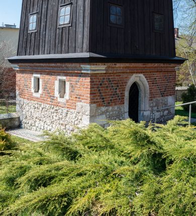 Zdjęcie nr 44: Kościół murowany z cegły, z użyciem zendrówki, na wysokim podmurowaniu z kamienia łupanego, jednonawowy, orientowany. 
Prezbiterium i nawa na planie prostokątów, nawa szersza i dłuższa od prezbiterium. Zakrystia na rzucie wydłużonego prostokąta przylega do wschodniej ściany prezbiterium, występując poza mury nawy. Prezbiterium od wschodu ujęte w narożach dwiema ukośnymi szkarpami, od południa jedną prostopadłą. Przy południowej ścianie nawy kruchta na planie kwadratu. Nawa w narożach ujęta szkarpami, od wschodu dwiema prostopadłymi, od zachodu ukośnymi. 
Prezbiterium dwuprzęsłowe, nakryte sklepieniem krzyżowo-żebrowym. Na zwornikach dwie tarcze z herbami Trzy Korony i Wieniawa. Zakrystia sklepiona kolebkowo. Nawa nakryta drewnianym stropem z kasetonami i rozetami. Kruchta sklepiona krzyżowo-żebrowo ze zwornikiem z tarczą z herbem Wieniawa. Otwór tęczowy w formie stojącego prostokąta zamkniętego łukiem ostrym. W zachodniej części nawy drewniany parapet chóru muzycznego wsparty na dwóch filarach. 
Fasada w jednej trzeciej wysokości odcięta kamiennym gzymsem kapnikowym, zakończona jodełkowym fryzem w partii muru, zwieńczona trójkątnym szczytem. Mur dekorowany zendrówką ułożoną „w zęby”, w partii szczytu w układzie rombowym. Na osi kamienny ostrołukowy portal o schodkowym nadprożu, dekorowanym krzyżującym się laskowaniem; węgary gładkie w jednej trzeciej wysokości przechodzące w piramidki i profilowanie powyżej. Nad portalem kamienna kwadratowa tablica, ujęta kamiennym obramieniem z tarczą z herbem Wieniawa. Ponad nią, na osi okulus w kamiennym obramieniu. 
Elewacje północna i południowa w części nawy w jednej trzeciej wysokości przedzielone kamiennym gzymsem kapnikowym, na zakończeniu ścian z gzymsem wieńczącym. Mur dekorowany zendrówką w układzie rombowym. Na elewacji południowej cztery okna w formie wydłużonego, stojącego prostokąta zamkniętego łukiem ostrym, w kamiennych obramieniach, podzielone laskowaniem. Południowa ściana prezbiterium zakończona gzymsem wieńczącym, w górnej części muru dekorowana zendrówką ułożoną „w zęby”. 
Szkarpy opinające nawę uskokowe, zwężające się ku górze, nakryte daszkami pulpitowymi. Szkarpy opinające prezbiterium nakryte daszkami pulpitowymi, podzielone gzymsami kapnikowymi. 
Kruchta od strony wschodniej i zachodniej podzielona kamiennym gzymsem kapnikowym, od południa zakończona gzymsem wieńczącym. Na ścianie południowej kruchty kamienny, ostrołukowy portal, o schodkowym nadprożu, dekorowanym krzyżującym się laskowaniem; węgary gładkie, w jednej trzeciej wysokości przechodzące w piramidki i profilowanie powyżej. Nad portalem kamienna tarcza z herbem Wieniawa. 
Elewacja wschodnia zwieńczona trójkątnym szczytem, w którego partii mur dekorowany jest zendrówką w układzie rombowym. Na osi okno w formie wydłużonego, stojącego prostokąta zamkniętego łukiem ostrym, w kamiennym obramieniu, zamurowane w trzech piątych wysokości, zakończone daszkiem pulpitowym. W dolnej części okna znajduje się ogrójec. 
Nawa i prezbiterium nakryte osobnymi blaszanymi dachami dwuspadowymi, kruchta i zakrystia pulpitowymi. Nad nawą blaszana wieżyczka na sygnaturkę z latarnią i hełmem baniastym.





