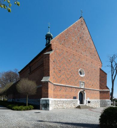 Zdjęcie nr 30: Kościół murowany z cegły, z użyciem zendrówki, na wysokim podmurowaniu z kamienia łupanego, jednonawowy, orientowany. 
Prezbiterium i nawa na planie prostokątów, nawa szersza i dłuższa od prezbiterium. Zakrystia na rzucie wydłużonego prostokąta przylega do wschodniej ściany prezbiterium, występując poza mury nawy. Prezbiterium od wschodu ujęte w narożach dwiema ukośnymi szkarpami, od południa jedną prostopadłą. Przy południowej ścianie nawy kruchta na planie kwadratu. Nawa w narożach ujęta szkarpami, od wschodu dwiema prostopadłymi, od zachodu ukośnymi. 
Prezbiterium dwuprzęsłowe, nakryte sklepieniem krzyżowo-żebrowym. Na zwornikach dwie tarcze z herbami Trzy Korony i Wieniawa. Zakrystia sklepiona kolebkowo. Nawa nakryta drewnianym stropem z kasetonami i rozetami. Kruchta sklepiona krzyżowo-żebrowo ze zwornikiem z tarczą z herbem Wieniawa. Otwór tęczowy w formie stojącego prostokąta zamkniętego łukiem ostrym. W zachodniej części nawy drewniany parapet chóru muzycznego wsparty na dwóch filarach. 
Fasada w jednej trzeciej wysokości odcięta kamiennym gzymsem kapnikowym, zakończona jodełkowym fryzem w partii muru, zwieńczona trójkątnym szczytem. Mur dekorowany zendrówką ułożoną „w zęby”, w partii szczytu w układzie rombowym. Na osi kamienny ostrołukowy portal o schodkowym nadprożu, dekorowanym krzyżującym się laskowaniem; węgary gładkie w jednej trzeciej wysokości przechodzące w piramidki i profilowanie powyżej. Nad portalem kamienna kwadratowa tablica, ujęta kamiennym obramieniem z tarczą z herbem Wieniawa. Ponad nią, na osi okulus w kamiennym obramieniu. 
Elewacje północna i południowa w części nawy w jednej trzeciej wysokości przedzielone kamiennym gzymsem kapnikowym, na zakończeniu ścian z gzymsem wieńczącym. Mur dekorowany zendrówką w układzie rombowym. Na elewacji południowej cztery okna w formie wydłużonego, stojącego prostokąta zamkniętego łukiem ostrym, w kamiennych obramieniach, podzielone laskowaniem. Południowa ściana prezbiterium zakończona gzymsem wieńczącym, w górnej części muru dekorowana zendrówką ułożoną „w zęby”. 
Szkarpy opinające nawę uskokowe, zwężające się ku górze, nakryte daszkami pulpitowymi. Szkarpy opinające prezbiterium nakryte daszkami pulpitowymi, podzielone gzymsami kapnikowymi. 
Kruchta od strony wschodniej i zachodniej podzielona kamiennym gzymsem kapnikowym, od południa zakończona gzymsem wieńczącym. Na ścianie południowej kruchty kamienny, ostrołukowy portal, o schodkowym nadprożu, dekorowanym krzyżującym się laskowaniem; węgary gładkie, w jednej trzeciej wysokości przechodzące w piramidki i profilowanie powyżej. Nad portalem kamienna tarcza z herbem Wieniawa. 
Elewacja wschodnia zwieńczona trójkątnym szczytem, w którego partii mur dekorowany jest zendrówką w układzie rombowym. Na osi okno w formie wydłużonego, stojącego prostokąta zamkniętego łukiem ostrym, w kamiennym obramieniu, zamurowane w trzech piątych wysokości, zakończone daszkiem pulpitowym. W dolnej części okna znajduje się ogrójec. 
Nawa i prezbiterium nakryte osobnymi blaszanymi dachami dwuspadowymi, kruchta i zakrystia pulpitowymi. Nad nawą blaszana wieżyczka na sygnaturkę z latarnią i hełmem baniastym.





