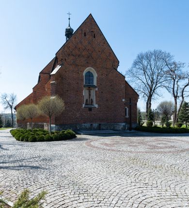 Zdjęcie nr 32: Kościół murowany z cegły, z użyciem zendrówki, na wysokim podmurowaniu z kamienia łupanego, jednonawowy, orientowany. 
Prezbiterium i nawa na planie prostokątów, nawa szersza i dłuższa od prezbiterium. Zakrystia na rzucie wydłużonego prostokąta przylega do wschodniej ściany prezbiterium, występując poza mury nawy. Prezbiterium od wschodu ujęte w narożach dwiema ukośnymi szkarpami, od południa jedną prostopadłą. Przy południowej ścianie nawy kruchta na planie kwadratu. Nawa w narożach ujęta szkarpami, od wschodu dwiema prostopadłymi, od zachodu ukośnymi. 
Prezbiterium dwuprzęsłowe, nakryte sklepieniem krzyżowo-żebrowym. Na zwornikach dwie tarcze z herbami Trzy Korony i Wieniawa. Zakrystia sklepiona kolebkowo. Nawa nakryta drewnianym stropem z kasetonami i rozetami. Kruchta sklepiona krzyżowo-żebrowo ze zwornikiem z tarczą z herbem Wieniawa. Otwór tęczowy w formie stojącego prostokąta zamkniętego łukiem ostrym. W zachodniej części nawy drewniany parapet chóru muzycznego wsparty na dwóch filarach. 
Fasada w jednej trzeciej wysokości odcięta kamiennym gzymsem kapnikowym, zakończona jodełkowym fryzem w partii muru, zwieńczona trójkątnym szczytem. Mur dekorowany zendrówką ułożoną „w zęby”, w partii szczytu w układzie rombowym. Na osi kamienny ostrołukowy portal o schodkowym nadprożu, dekorowanym krzyżującym się laskowaniem; węgary gładkie w jednej trzeciej wysokości przechodzące w piramidki i profilowanie powyżej. Nad portalem kamienna kwadratowa tablica, ujęta kamiennym obramieniem z tarczą z herbem Wieniawa. Ponad nią, na osi okulus w kamiennym obramieniu. 
Elewacje północna i południowa w części nawy w jednej trzeciej wysokości przedzielone kamiennym gzymsem kapnikowym, na zakończeniu ścian z gzymsem wieńczącym. Mur dekorowany zendrówką w układzie rombowym. Na elewacji południowej cztery okna w formie wydłużonego, stojącego prostokąta zamkniętego łukiem ostrym, w kamiennych obramieniach, podzielone laskowaniem. Południowa ściana prezbiterium zakończona gzymsem wieńczącym, w górnej części muru dekorowana zendrówką ułożoną „w zęby”. 
Szkarpy opinające nawę uskokowe, zwężające się ku górze, nakryte daszkami pulpitowymi. Szkarpy opinające prezbiterium nakryte daszkami pulpitowymi, podzielone gzymsami kapnikowymi. 
Kruchta od strony wschodniej i zachodniej podzielona kamiennym gzymsem kapnikowym, od południa zakończona gzymsem wieńczącym. Na ścianie południowej kruchty kamienny, ostrołukowy portal, o schodkowym nadprożu, dekorowanym krzyżującym się laskowaniem; węgary gładkie, w jednej trzeciej wysokości przechodzące w piramidki i profilowanie powyżej. Nad portalem kamienna tarcza z herbem Wieniawa. 
Elewacja wschodnia zwieńczona trójkątnym szczytem, w którego partii mur dekorowany jest zendrówką w układzie rombowym. Na osi okno w formie wydłużonego, stojącego prostokąta zamkniętego łukiem ostrym, w kamiennym obramieniu, zamurowane w trzech piątych wysokości, zakończone daszkiem pulpitowym. W dolnej części okna znajduje się ogrójec. 
Nawa i prezbiterium nakryte osobnymi blaszanymi dachami dwuspadowymi, kruchta i zakrystia pulpitowymi. Nad nawą blaszana wieżyczka na sygnaturkę z latarnią i hełmem baniastym.





