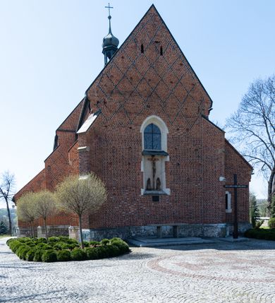 Zdjęcie nr 34: Kościół murowany z cegły, z użyciem zendrówki, na wysokim podmurowaniu z kamienia łupanego, jednonawowy, orientowany. 
Prezbiterium i nawa na planie prostokątów, nawa szersza i dłuższa od prezbiterium. Zakrystia na rzucie wydłużonego prostokąta przylega do wschodniej ściany prezbiterium, występując poza mury nawy. Prezbiterium od wschodu ujęte w narożach dwiema ukośnymi szkarpami, od południa jedną prostopadłą. Przy południowej ścianie nawy kruchta na planie kwadratu. Nawa w narożach ujęta szkarpami, od wschodu dwiema prostopadłymi, od zachodu ukośnymi. 
Prezbiterium dwuprzęsłowe, nakryte sklepieniem krzyżowo-żebrowym. Na zwornikach dwie tarcze z herbami Trzy Korony i Wieniawa. Zakrystia sklepiona kolebkowo. Nawa nakryta drewnianym stropem z kasetonami i rozetami. Kruchta sklepiona krzyżowo-żebrowo ze zwornikiem z tarczą z herbem Wieniawa. Otwór tęczowy w formie stojącego prostokąta zamkniętego łukiem ostrym. W zachodniej części nawy drewniany parapet chóru muzycznego wsparty na dwóch filarach. 
Fasada w jednej trzeciej wysokości odcięta kamiennym gzymsem kapnikowym, zakończona jodełkowym fryzem w partii muru, zwieńczona trójkątnym szczytem. Mur dekorowany zendrówką ułożoną „w zęby”, w partii szczytu w układzie rombowym. Na osi kamienny ostrołukowy portal o schodkowym nadprożu, dekorowanym krzyżującym się laskowaniem; węgary gładkie w jednej trzeciej wysokości przechodzące w piramidki i profilowanie powyżej. Nad portalem kamienna kwadratowa tablica, ujęta kamiennym obramieniem z tarczą z herbem Wieniawa. Ponad nią, na osi okulus w kamiennym obramieniu. 
Elewacje północna i południowa w części nawy w jednej trzeciej wysokości przedzielone kamiennym gzymsem kapnikowym, na zakończeniu ścian z gzymsem wieńczącym. Mur dekorowany zendrówką w układzie rombowym. Na elewacji południowej cztery okna w formie wydłużonego, stojącego prostokąta zamkniętego łukiem ostrym, w kamiennych obramieniach, podzielone laskowaniem. Południowa ściana prezbiterium zakończona gzymsem wieńczącym, w górnej części muru dekorowana zendrówką ułożoną „w zęby”. 
Szkarpy opinające nawę uskokowe, zwężające się ku górze, nakryte daszkami pulpitowymi. Szkarpy opinające prezbiterium nakryte daszkami pulpitowymi, podzielone gzymsami kapnikowymi. 
Kruchta od strony wschodniej i zachodniej podzielona kamiennym gzymsem kapnikowym, od południa zakończona gzymsem wieńczącym. Na ścianie południowej kruchty kamienny, ostrołukowy portal, o schodkowym nadprożu, dekorowanym krzyżującym się laskowaniem; węgary gładkie, w jednej trzeciej wysokości przechodzące w piramidki i profilowanie powyżej. Nad portalem kamienna tarcza z herbem Wieniawa. 
Elewacja wschodnia zwieńczona trójkątnym szczytem, w którego partii mur dekorowany jest zendrówką w układzie rombowym. Na osi okno w formie wydłużonego, stojącego prostokąta zamkniętego łukiem ostrym, w kamiennym obramieniu, zamurowane w trzech piątych wysokości, zakończone daszkiem pulpitowym. W dolnej części okna znajduje się ogrójec. 
Nawa i prezbiterium nakryte osobnymi blaszanymi dachami dwuspadowymi, kruchta i zakrystia pulpitowymi. Nad nawą blaszana wieżyczka na sygnaturkę z latarnią i hełmem baniastym.





