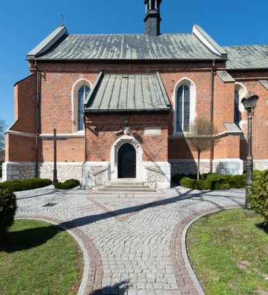 Zdjęcie nr 37: Kościół murowany z cegły, z użyciem zendrówki, na wysokim podmurowaniu z kamienia łupanego, jednonawowy, orientowany. 
Prezbiterium i nawa na planie prostokątów, nawa szersza i dłuższa od prezbiterium. Zakrystia na rzucie wydłużonego prostokąta przylega do wschodniej ściany prezbiterium, występując poza mury nawy. Prezbiterium od wschodu ujęte w narożach dwiema ukośnymi szkarpami, od południa jedną prostopadłą. Przy południowej ścianie nawy kruchta na planie kwadratu. Nawa w narożach ujęta szkarpami, od wschodu dwiema prostopadłymi, od zachodu ukośnymi. 
Prezbiterium dwuprzęsłowe, nakryte sklepieniem krzyżowo-żebrowym. Na zwornikach dwie tarcze z herbami Trzy Korony i Wieniawa. Zakrystia sklepiona kolebkowo. Nawa nakryta drewnianym stropem z kasetonami i rozetami. Kruchta sklepiona krzyżowo-żebrowo ze zwornikiem z tarczą z herbem Wieniawa. Otwór tęczowy w formie stojącego prostokąta zamkniętego łukiem ostrym. W zachodniej części nawy drewniany parapet chóru muzycznego wsparty na dwóch filarach. 
Fasada w jednej trzeciej wysokości odcięta kamiennym gzymsem kapnikowym, zakończona jodełkowym fryzem w partii muru, zwieńczona trójkątnym szczytem. Mur dekorowany zendrówką ułożoną „w zęby”, w partii szczytu w układzie rombowym. Na osi kamienny ostrołukowy portal o schodkowym nadprożu, dekorowanym krzyżującym się laskowaniem; węgary gładkie w jednej trzeciej wysokości przechodzące w piramidki i profilowanie powyżej. Nad portalem kamienna kwadratowa tablica, ujęta kamiennym obramieniem z tarczą z herbem Wieniawa. Ponad nią, na osi okulus w kamiennym obramieniu. 
Elewacje północna i południowa w części nawy w jednej trzeciej wysokości przedzielone kamiennym gzymsem kapnikowym, na zakończeniu ścian z gzymsem wieńczącym. Mur dekorowany zendrówką w układzie rombowym. Na elewacji południowej cztery okna w formie wydłużonego, stojącego prostokąta zamkniętego łukiem ostrym, w kamiennych obramieniach, podzielone laskowaniem. Południowa ściana prezbiterium zakończona gzymsem wieńczącym, w górnej części muru dekorowana zendrówką ułożoną „w zęby”. 
Szkarpy opinające nawę uskokowe, zwężające się ku górze, nakryte daszkami pulpitowymi. Szkarpy opinające prezbiterium nakryte daszkami pulpitowymi, podzielone gzymsami kapnikowymi. 
Kruchta od strony wschodniej i zachodniej podzielona kamiennym gzymsem kapnikowym, od południa zakończona gzymsem wieńczącym. Na ścianie południowej kruchty kamienny, ostrołukowy portal, o schodkowym nadprożu, dekorowanym krzyżującym się laskowaniem; węgary gładkie, w jednej trzeciej wysokości przechodzące w piramidki i profilowanie powyżej. Nad portalem kamienna tarcza z herbem Wieniawa. 
Elewacja wschodnia zwieńczona trójkątnym szczytem, w którego partii mur dekorowany jest zendrówką w układzie rombowym. Na osi okno w formie wydłużonego, stojącego prostokąta zamkniętego łukiem ostrym, w kamiennym obramieniu, zamurowane w trzech piątych wysokości, zakończone daszkiem pulpitowym. W dolnej części okna znajduje się ogrójec. 
Nawa i prezbiterium nakryte osobnymi blaszanymi dachami dwuspadowymi, kruchta i zakrystia pulpitowymi. Nad nawą blaszana wieżyczka na sygnaturkę z latarnią i hełmem baniastym.





