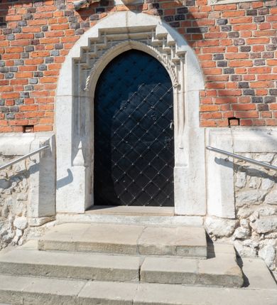 Zdjęcie nr 56: Kościół murowany z cegły, z użyciem zendrówki, na wysokim podmurowaniu z kamienia łupanego, jednonawowy, orientowany. 
Prezbiterium i nawa na planie prostokątów, nawa szersza i dłuższa od prezbiterium. Zakrystia na rzucie wydłużonego prostokąta przylega do wschodniej ściany prezbiterium, występując poza mury nawy. Prezbiterium od wschodu ujęte w narożach dwiema ukośnymi szkarpami, od południa jedną prostopadłą. Przy południowej ścianie nawy kruchta na planie kwadratu. Nawa w narożach ujęta szkarpami, od wschodu dwiema prostopadłymi, od zachodu ukośnymi. 
Prezbiterium dwuprzęsłowe, nakryte sklepieniem krzyżowo-żebrowym. Na zwornikach dwie tarcze z herbami Trzy Korony i Wieniawa. Zakrystia sklepiona kolebkowo. Nawa nakryta drewnianym stropem z kasetonami i rozetami. Kruchta sklepiona krzyżowo-żebrowo ze zwornikiem z tarczą z herbem Wieniawa. Otwór tęczowy w formie stojącego prostokąta zamkniętego łukiem ostrym. W zachodniej części nawy drewniany parapet chóru muzycznego wsparty na dwóch filarach. 
Fasada w jednej trzeciej wysokości odcięta kamiennym gzymsem kapnikowym, zakończona jodełkowym fryzem w partii muru, zwieńczona trójkątnym szczytem. Mur dekorowany zendrówką ułożoną „w zęby”, w partii szczytu w układzie rombowym. Na osi kamienny ostrołukowy portal o schodkowym nadprożu, dekorowanym krzyżującym się laskowaniem; węgary gładkie w jednej trzeciej wysokości przechodzące w piramidki i profilowanie powyżej. Nad portalem kamienna kwadratowa tablica, ujęta kamiennym obramieniem z tarczą z herbem Wieniawa. Ponad nią, na osi okulus w kamiennym obramieniu. 
Elewacje północna i południowa w części nawy w jednej trzeciej wysokości przedzielone kamiennym gzymsem kapnikowym, na zakończeniu ścian z gzymsem wieńczącym. Mur dekorowany zendrówką w układzie rombowym. Na elewacji południowej cztery okna w formie wydłużonego, stojącego prostokąta zamkniętego łukiem ostrym, w kamiennych obramieniach, podzielone laskowaniem. Południowa ściana prezbiterium zakończona gzymsem wieńczącym, w górnej części muru dekorowana zendrówką ułożoną „w zęby”. 
Szkarpy opinające nawę uskokowe, zwężające się ku górze, nakryte daszkami pulpitowymi. Szkarpy opinające prezbiterium nakryte daszkami pulpitowymi, podzielone gzymsami kapnikowymi. 
Kruchta od strony wschodniej i zachodniej podzielona kamiennym gzymsem kapnikowym, od południa zakończona gzymsem wieńczącym. Na ścianie południowej kruchty kamienny, ostrołukowy portal, o schodkowym nadprożu, dekorowanym krzyżującym się laskowaniem; węgary gładkie, w jednej trzeciej wysokości przechodzące w piramidki i profilowanie powyżej. Nad portalem kamienna tarcza z herbem Wieniawa. 
Elewacja wschodnia zwieńczona trójkątnym szczytem, w którego partii mur dekorowany jest zendrówką w układzie rombowym. Na osi okno w formie wydłużonego, stojącego prostokąta zamkniętego łukiem ostrym, w kamiennym obramieniu, zamurowane w trzech piątych wysokości, zakończone daszkiem pulpitowym. W dolnej części okna znajduje się ogrójec. 
Nawa i prezbiterium nakryte osobnymi blaszanymi dachami dwuspadowymi, kruchta i zakrystia pulpitowymi. Nad nawą blaszana wieżyczka na sygnaturkę z latarnią i hełmem baniastym.





