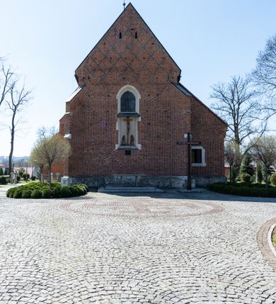 Zdjęcie nr 33: Kościół murowany z cegły, z użyciem zendrówki, na wysokim podmurowaniu z kamienia łupanego, jednonawowy, orientowany. 
Prezbiterium i nawa na planie prostokątów, nawa szersza i dłuższa od prezbiterium. Zakrystia na rzucie wydłużonego prostokąta przylega do wschodniej ściany prezbiterium, występując poza mury nawy. Prezbiterium od wschodu ujęte w narożach dwiema ukośnymi szkarpami, od południa jedną prostopadłą. Przy południowej ścianie nawy kruchta na planie kwadratu. Nawa w narożach ujęta szkarpami, od wschodu dwiema prostopadłymi, od zachodu ukośnymi. 
Prezbiterium dwuprzęsłowe, nakryte sklepieniem krzyżowo-żebrowym. Na zwornikach dwie tarcze z herbami Trzy Korony i Wieniawa. Zakrystia sklepiona kolebkowo. Nawa nakryta drewnianym stropem z kasetonami i rozetami. Kruchta sklepiona krzyżowo-żebrowo ze zwornikiem z tarczą z herbem Wieniawa. Otwór tęczowy w formie stojącego prostokąta zamkniętego łukiem ostrym. W zachodniej części nawy drewniany parapet chóru muzycznego wsparty na dwóch filarach. 
Fasada w jednej trzeciej wysokości odcięta kamiennym gzymsem kapnikowym, zakończona jodełkowym fryzem w partii muru, zwieńczona trójkątnym szczytem. Mur dekorowany zendrówką ułożoną „w zęby”, w partii szczytu w układzie rombowym. Na osi kamienny ostrołukowy portal o schodkowym nadprożu, dekorowanym krzyżującym się laskowaniem; węgary gładkie w jednej trzeciej wysokości przechodzące w piramidki i profilowanie powyżej. Nad portalem kamienna kwadratowa tablica, ujęta kamiennym obramieniem z tarczą z herbem Wieniawa. Ponad nią, na osi okulus w kamiennym obramieniu. 
Elewacje północna i południowa w części nawy w jednej trzeciej wysokości przedzielone kamiennym gzymsem kapnikowym, na zakończeniu ścian z gzymsem wieńczącym. Mur dekorowany zendrówką w układzie rombowym. Na elewacji południowej cztery okna w formie wydłużonego, stojącego prostokąta zamkniętego łukiem ostrym, w kamiennych obramieniach, podzielone laskowaniem. Południowa ściana prezbiterium zakończona gzymsem wieńczącym, w górnej części muru dekorowana zendrówką ułożoną „w zęby”. 
Szkarpy opinające nawę uskokowe, zwężające się ku górze, nakryte daszkami pulpitowymi. Szkarpy opinające prezbiterium nakryte daszkami pulpitowymi, podzielone gzymsami kapnikowymi. 
Kruchta od strony wschodniej i zachodniej podzielona kamiennym gzymsem kapnikowym, od południa zakończona gzymsem wieńczącym. Na ścianie południowej kruchty kamienny, ostrołukowy portal, o schodkowym nadprożu, dekorowanym krzyżującym się laskowaniem; węgary gładkie, w jednej trzeciej wysokości przechodzące w piramidki i profilowanie powyżej. Nad portalem kamienna tarcza z herbem Wieniawa. 
Elewacja wschodnia zwieńczona trójkątnym szczytem, w którego partii mur dekorowany jest zendrówką w układzie rombowym. Na osi okno w formie wydłużonego, stojącego prostokąta zamkniętego łukiem ostrym, w kamiennym obramieniu, zamurowane w trzech piątych wysokości, zakończone daszkiem pulpitowym. W dolnej części okna znajduje się ogrójec. 
Nawa i prezbiterium nakryte osobnymi blaszanymi dachami dwuspadowymi, kruchta i zakrystia pulpitowymi. Nad nawą blaszana wieżyczka na sygnaturkę z latarnią i hełmem baniastym.





