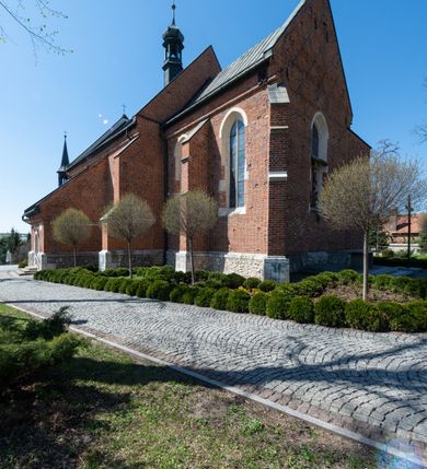 Zdjęcie nr 40: Kościół murowany z cegły, z użyciem zendrówki, na wysokim podmurowaniu z kamienia łupanego, jednonawowy, orientowany. 
Prezbiterium i nawa na planie prostokątów, nawa szersza i dłuższa od prezbiterium. Zakrystia na rzucie wydłużonego prostokąta przylega do wschodniej ściany prezbiterium, występując poza mury nawy. Prezbiterium od wschodu ujęte w narożach dwiema ukośnymi szkarpami, od południa jedną prostopadłą. Przy południowej ścianie nawy kruchta na planie kwadratu. Nawa w narożach ujęta szkarpami, od wschodu dwiema prostopadłymi, od zachodu ukośnymi. 
Prezbiterium dwuprzęsłowe, nakryte sklepieniem krzyżowo-żebrowym. Na zwornikach dwie tarcze z herbami Trzy Korony i Wieniawa. Zakrystia sklepiona kolebkowo. Nawa nakryta drewnianym stropem z kasetonami i rozetami. Kruchta sklepiona krzyżowo-żebrowo ze zwornikiem z tarczą z herbem Wieniawa. Otwór tęczowy w formie stojącego prostokąta zamkniętego łukiem ostrym. W zachodniej części nawy drewniany parapet chóru muzycznego wsparty na dwóch filarach. 
Fasada w jednej trzeciej wysokości odcięta kamiennym gzymsem kapnikowym, zakończona jodełkowym fryzem w partii muru, zwieńczona trójkątnym szczytem. Mur dekorowany zendrówką ułożoną „w zęby”, w partii szczytu w układzie rombowym. Na osi kamienny ostrołukowy portal o schodkowym nadprożu, dekorowanym krzyżującym się laskowaniem; węgary gładkie w jednej trzeciej wysokości przechodzące w piramidki i profilowanie powyżej. Nad portalem kamienna kwadratowa tablica, ujęta kamiennym obramieniem z tarczą z herbem Wieniawa. Ponad nią, na osi okulus w kamiennym obramieniu. 
Elewacje północna i południowa w części nawy w jednej trzeciej wysokości przedzielone kamiennym gzymsem kapnikowym, na zakończeniu ścian z gzymsem wieńczącym. Mur dekorowany zendrówką w układzie rombowym. Na elewacji południowej cztery okna w formie wydłużonego, stojącego prostokąta zamkniętego łukiem ostrym, w kamiennych obramieniach, podzielone laskowaniem. Południowa ściana prezbiterium zakończona gzymsem wieńczącym, w górnej części muru dekorowana zendrówką ułożoną „w zęby”. 
Szkarpy opinające nawę uskokowe, zwężające się ku górze, nakryte daszkami pulpitowymi. Szkarpy opinające prezbiterium nakryte daszkami pulpitowymi, podzielone gzymsami kapnikowymi. 
Kruchta od strony wschodniej i zachodniej podzielona kamiennym gzymsem kapnikowym, od południa zakończona gzymsem wieńczącym. Na ścianie południowej kruchty kamienny, ostrołukowy portal, o schodkowym nadprożu, dekorowanym krzyżującym się laskowaniem; węgary gładkie, w jednej trzeciej wysokości przechodzące w piramidki i profilowanie powyżej. Nad portalem kamienna tarcza z herbem Wieniawa. 
Elewacja wschodnia zwieńczona trójkątnym szczytem, w którego partii mur dekorowany jest zendrówką w układzie rombowym. Na osi okno w formie wydłużonego, stojącego prostokąta zamkniętego łukiem ostrym, w kamiennym obramieniu, zamurowane w trzech piątych wysokości, zakończone daszkiem pulpitowym. W dolnej części okna znajduje się ogrójec. 
Nawa i prezbiterium nakryte osobnymi blaszanymi dachami dwuspadowymi, kruchta i zakrystia pulpitowymi. Nad nawą blaszana wieżyczka na sygnaturkę z latarnią i hełmem baniastym.





