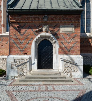 Zdjęcie nr 57: Kościół murowany z cegły, z użyciem zendrówki, na wysokim podmurowaniu z kamienia łupanego, jednonawowy, orientowany. 
Prezbiterium i nawa na planie prostokątów, nawa szersza i dłuższa od prezbiterium. Zakrystia na rzucie wydłużonego prostokąta przylega do wschodniej ściany prezbiterium, występując poza mury nawy. Prezbiterium od wschodu ujęte w narożach dwiema ukośnymi szkarpami, od południa jedną prostopadłą. Przy południowej ścianie nawy kruchta na planie kwadratu. Nawa w narożach ujęta szkarpami, od wschodu dwiema prostopadłymi, od zachodu ukośnymi. 
Prezbiterium dwuprzęsłowe, nakryte sklepieniem krzyżowo-żebrowym. Na zwornikach dwie tarcze z herbami Trzy Korony i Wieniawa. Zakrystia sklepiona kolebkowo. Nawa nakryta drewnianym stropem z kasetonami i rozetami. Kruchta sklepiona krzyżowo-żebrowo ze zwornikiem z tarczą z herbem Wieniawa. Otwór tęczowy w formie stojącego prostokąta zamkniętego łukiem ostrym. W zachodniej części nawy drewniany parapet chóru muzycznego wsparty na dwóch filarach. 
Fasada w jednej trzeciej wysokości odcięta kamiennym gzymsem kapnikowym, zakończona jodełkowym fryzem w partii muru, zwieńczona trójkątnym szczytem. Mur dekorowany zendrówką ułożoną „w zęby”, w partii szczytu w układzie rombowym. Na osi kamienny ostrołukowy portal o schodkowym nadprożu, dekorowanym krzyżującym się laskowaniem; węgary gładkie w jednej trzeciej wysokości przechodzące w piramidki i profilowanie powyżej. Nad portalem kamienna kwadratowa tablica, ujęta kamiennym obramieniem z tarczą z herbem Wieniawa. Ponad nią, na osi okulus w kamiennym obramieniu. 
Elewacje północna i południowa w części nawy w jednej trzeciej wysokości przedzielone kamiennym gzymsem kapnikowym, na zakończeniu ścian z gzymsem wieńczącym. Mur dekorowany zendrówką w układzie rombowym. Na elewacji południowej cztery okna w formie wydłużonego, stojącego prostokąta zamkniętego łukiem ostrym, w kamiennych obramieniach, podzielone laskowaniem. Południowa ściana prezbiterium zakończona gzymsem wieńczącym, w górnej części muru dekorowana zendrówką ułożoną „w zęby”. 
Szkarpy opinające nawę uskokowe, zwężające się ku górze, nakryte daszkami pulpitowymi. Szkarpy opinające prezbiterium nakryte daszkami pulpitowymi, podzielone gzymsami kapnikowymi. 
Kruchta od strony wschodniej i zachodniej podzielona kamiennym gzymsem kapnikowym, od południa zakończona gzymsem wieńczącym. Na ścianie południowej kruchty kamienny, ostrołukowy portal, o schodkowym nadprożu, dekorowanym krzyżującym się laskowaniem; węgary gładkie, w jednej trzeciej wysokości przechodzące w piramidki i profilowanie powyżej. Nad portalem kamienna tarcza z herbem Wieniawa. 
Elewacja wschodnia zwieńczona trójkątnym szczytem, w którego partii mur dekorowany jest zendrówką w układzie rombowym. Na osi okno w formie wydłużonego, stojącego prostokąta zamkniętego łukiem ostrym, w kamiennym obramieniu, zamurowane w trzech piątych wysokości, zakończone daszkiem pulpitowym. W dolnej części okna znajduje się ogrójec. 
Nawa i prezbiterium nakryte osobnymi blaszanymi dachami dwuspadowymi, kruchta i zakrystia pulpitowymi. Nad nawą blaszana wieżyczka na sygnaturkę z latarnią i hełmem baniastym.





