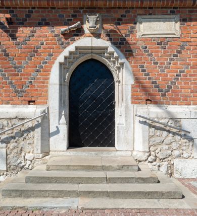 Zdjęcie nr 60: Kościół murowany z cegły, z użyciem zendrówki, na wysokim podmurowaniu z kamienia łupanego, jednonawowy, orientowany. 
Prezbiterium i nawa na planie prostokątów, nawa szersza i dłuższa od prezbiterium. Zakrystia na rzucie wydłużonego prostokąta przylega do wschodniej ściany prezbiterium, występując poza mury nawy. Prezbiterium od wschodu ujęte w narożach dwiema ukośnymi szkarpami, od południa jedną prostopadłą. Przy południowej ścianie nawy kruchta na planie kwadratu. Nawa w narożach ujęta szkarpami, od wschodu dwiema prostopadłymi, od zachodu ukośnymi. 
Prezbiterium dwuprzęsłowe, nakryte sklepieniem krzyżowo-żebrowym. Na zwornikach dwie tarcze z herbami Trzy Korony i Wieniawa. Zakrystia sklepiona kolebkowo. Nawa nakryta drewnianym stropem z kasetonami i rozetami. Kruchta sklepiona krzyżowo-żebrowo ze zwornikiem z tarczą z herbem Wieniawa. Otwór tęczowy w formie stojącego prostokąta zamkniętego łukiem ostrym. W zachodniej części nawy drewniany parapet chóru muzycznego wsparty na dwóch filarach. 
Fasada w jednej trzeciej wysokości odcięta kamiennym gzymsem kapnikowym, zakończona jodełkowym fryzem w partii muru, zwieńczona trójkątnym szczytem. Mur dekorowany zendrówką ułożoną „w zęby”, w partii szczytu w układzie rombowym. Na osi kamienny ostrołukowy portal o schodkowym nadprożu, dekorowanym krzyżującym się laskowaniem; węgary gładkie w jednej trzeciej wysokości przechodzące w piramidki i profilowanie powyżej. Nad portalem kamienna kwadratowa tablica, ujęta kamiennym obramieniem z tarczą z herbem Wieniawa. Ponad nią, na osi okulus w kamiennym obramieniu. 
Elewacje północna i południowa w części nawy w jednej trzeciej wysokości przedzielone kamiennym gzymsem kapnikowym, na zakończeniu ścian z gzymsem wieńczącym. Mur dekorowany zendrówką w układzie rombowym. Na elewacji południowej cztery okna w formie wydłużonego, stojącego prostokąta zamkniętego łukiem ostrym, w kamiennych obramieniach, podzielone laskowaniem. Południowa ściana prezbiterium zakończona gzymsem wieńczącym, w górnej części muru dekorowana zendrówką ułożoną „w zęby”. 
Szkarpy opinające nawę uskokowe, zwężające się ku górze, nakryte daszkami pulpitowymi. Szkarpy opinające prezbiterium nakryte daszkami pulpitowymi, podzielone gzymsami kapnikowymi. 
Kruchta od strony wschodniej i zachodniej podzielona kamiennym gzymsem kapnikowym, od południa zakończona gzymsem wieńczącym. Na ścianie południowej kruchty kamienny, ostrołukowy portal, o schodkowym nadprożu, dekorowanym krzyżującym się laskowaniem; węgary gładkie, w jednej trzeciej wysokości przechodzące w piramidki i profilowanie powyżej. Nad portalem kamienna tarcza z herbem Wieniawa. 
Elewacja wschodnia zwieńczona trójkątnym szczytem, w którego partii mur dekorowany jest zendrówką w układzie rombowym. Na osi okno w formie wydłużonego, stojącego prostokąta zamkniętego łukiem ostrym, w kamiennym obramieniu, zamurowane w trzech piątych wysokości, zakończone daszkiem pulpitowym. W dolnej części okna znajduje się ogrójec. 
Nawa i prezbiterium nakryte osobnymi blaszanymi dachami dwuspadowymi, kruchta i zakrystia pulpitowymi. Nad nawą blaszana wieżyczka na sygnaturkę z latarnią i hełmem baniastym.





