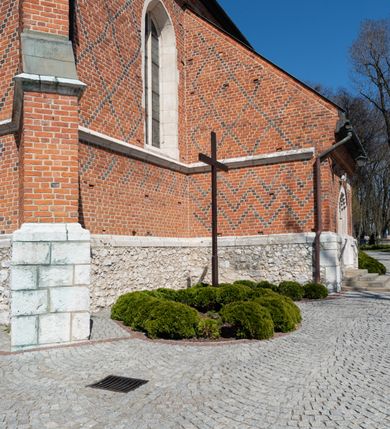 Zdjęcie nr 38: Kościół murowany z cegły, z użyciem zendrówki, na wysokim podmurowaniu z kamienia łupanego, jednonawowy, orientowany. 
Prezbiterium i nawa na planie prostokątów, nawa szersza i dłuższa od prezbiterium. Zakrystia na rzucie wydłużonego prostokąta przylega do wschodniej ściany prezbiterium, występując poza mury nawy. Prezbiterium od wschodu ujęte w narożach dwiema ukośnymi szkarpami, od południa jedną prostopadłą. Przy południowej ścianie nawy kruchta na planie kwadratu. Nawa w narożach ujęta szkarpami, od wschodu dwiema prostopadłymi, od zachodu ukośnymi. 
Prezbiterium dwuprzęsłowe, nakryte sklepieniem krzyżowo-żebrowym. Na zwornikach dwie tarcze z herbami Trzy Korony i Wieniawa. Zakrystia sklepiona kolebkowo. Nawa nakryta drewnianym stropem z kasetonami i rozetami. Kruchta sklepiona krzyżowo-żebrowo ze zwornikiem z tarczą z herbem Wieniawa. Otwór tęczowy w formie stojącego prostokąta zamkniętego łukiem ostrym. W zachodniej części nawy drewniany parapet chóru muzycznego wsparty na dwóch filarach. 
Fasada w jednej trzeciej wysokości odcięta kamiennym gzymsem kapnikowym, zakończona jodełkowym fryzem w partii muru, zwieńczona trójkątnym szczytem. Mur dekorowany zendrówką ułożoną „w zęby”, w partii szczytu w układzie rombowym. Na osi kamienny ostrołukowy portal o schodkowym nadprożu, dekorowanym krzyżującym się laskowaniem; węgary gładkie w jednej trzeciej wysokości przechodzące w piramidki i profilowanie powyżej. Nad portalem kamienna kwadratowa tablica, ujęta kamiennym obramieniem z tarczą z herbem Wieniawa. Ponad nią, na osi okulus w kamiennym obramieniu. 
Elewacje północna i południowa w części nawy w jednej trzeciej wysokości przedzielone kamiennym gzymsem kapnikowym, na zakończeniu ścian z gzymsem wieńczącym. Mur dekorowany zendrówką w układzie rombowym. Na elewacji południowej cztery okna w formie wydłużonego, stojącego prostokąta zamkniętego łukiem ostrym, w kamiennych obramieniach, podzielone laskowaniem. Południowa ściana prezbiterium zakończona gzymsem wieńczącym, w górnej części muru dekorowana zendrówką ułożoną „w zęby”. 
Szkarpy opinające nawę uskokowe, zwężające się ku górze, nakryte daszkami pulpitowymi. Szkarpy opinające prezbiterium nakryte daszkami pulpitowymi, podzielone gzymsami kapnikowymi. 
Kruchta od strony wschodniej i zachodniej podzielona kamiennym gzymsem kapnikowym, od południa zakończona gzymsem wieńczącym. Na ścianie południowej kruchty kamienny, ostrołukowy portal, o schodkowym nadprożu, dekorowanym krzyżującym się laskowaniem; węgary gładkie, w jednej trzeciej wysokości przechodzące w piramidki i profilowanie powyżej. Nad portalem kamienna tarcza z herbem Wieniawa. 
Elewacja wschodnia zwieńczona trójkątnym szczytem, w którego partii mur dekorowany jest zendrówką w układzie rombowym. Na osi okno w formie wydłużonego, stojącego prostokąta zamkniętego łukiem ostrym, w kamiennym obramieniu, zamurowane w trzech piątych wysokości, zakończone daszkiem pulpitowym. W dolnej części okna znajduje się ogrójec. 
Nawa i prezbiterium nakryte osobnymi blaszanymi dachami dwuspadowymi, kruchta i zakrystia pulpitowymi. Nad nawą blaszana wieżyczka na sygnaturkę z latarnią i hełmem baniastym.





