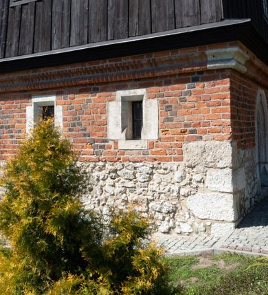 Zdjęcie nr 45: Kościół murowany z cegły, z użyciem zendrówki, na wysokim podmurowaniu z kamienia łupanego, jednonawowy, orientowany. 
Prezbiterium i nawa na planie prostokątów, nawa szersza i dłuższa od prezbiterium. Zakrystia na rzucie wydłużonego prostokąta przylega do wschodniej ściany prezbiterium, występując poza mury nawy. Prezbiterium od wschodu ujęte w narożach dwiema ukośnymi szkarpami, od południa jedną prostopadłą. Przy południowej ścianie nawy kruchta na planie kwadratu. Nawa w narożach ujęta szkarpami, od wschodu dwiema prostopadłymi, od zachodu ukośnymi. 
Prezbiterium dwuprzęsłowe, nakryte sklepieniem krzyżowo-żebrowym. Na zwornikach dwie tarcze z herbami Trzy Korony i Wieniawa. Zakrystia sklepiona kolebkowo. Nawa nakryta drewnianym stropem z kasetonami i rozetami. Kruchta sklepiona krzyżowo-żebrowo ze zwornikiem z tarczą z herbem Wieniawa. Otwór tęczowy w formie stojącego prostokąta zamkniętego łukiem ostrym. W zachodniej części nawy drewniany parapet chóru muzycznego wsparty na dwóch filarach. 
Fasada w jednej trzeciej wysokości odcięta kamiennym gzymsem kapnikowym, zakończona jodełkowym fryzem w partii muru, zwieńczona trójkątnym szczytem. Mur dekorowany zendrówką ułożoną „w zęby”, w partii szczytu w układzie rombowym. Na osi kamienny ostrołukowy portal o schodkowym nadprożu, dekorowanym krzyżującym się laskowaniem; węgary gładkie w jednej trzeciej wysokości przechodzące w piramidki i profilowanie powyżej. Nad portalem kamienna kwadratowa tablica, ujęta kamiennym obramieniem z tarczą z herbem Wieniawa. Ponad nią, na osi okulus w kamiennym obramieniu. 
Elewacje północna i południowa w części nawy w jednej trzeciej wysokości przedzielone kamiennym gzymsem kapnikowym, na zakończeniu ścian z gzymsem wieńczącym. Mur dekorowany zendrówką w układzie rombowym. Na elewacji południowej cztery okna w formie wydłużonego, stojącego prostokąta zamkniętego łukiem ostrym, w kamiennych obramieniach, podzielone laskowaniem. Południowa ściana prezbiterium zakończona gzymsem wieńczącym, w górnej części muru dekorowana zendrówką ułożoną „w zęby”. 
Szkarpy opinające nawę uskokowe, zwężające się ku górze, nakryte daszkami pulpitowymi. Szkarpy opinające prezbiterium nakryte daszkami pulpitowymi, podzielone gzymsami kapnikowymi. 
Kruchta od strony wschodniej i zachodniej podzielona kamiennym gzymsem kapnikowym, od południa zakończona gzymsem wieńczącym. Na ścianie południowej kruchty kamienny, ostrołukowy portal, o schodkowym nadprożu, dekorowanym krzyżującym się laskowaniem; węgary gładkie, w jednej trzeciej wysokości przechodzące w piramidki i profilowanie powyżej. Nad portalem kamienna tarcza z herbem Wieniawa. 
Elewacja wschodnia zwieńczona trójkątnym szczytem, w którego partii mur dekorowany jest zendrówką w układzie rombowym. Na osi okno w formie wydłużonego, stojącego prostokąta zamkniętego łukiem ostrym, w kamiennym obramieniu, zamurowane w trzech piątych wysokości, zakończone daszkiem pulpitowym. W dolnej części okna znajduje się ogrójec. 
Nawa i prezbiterium nakryte osobnymi blaszanymi dachami dwuspadowymi, kruchta i zakrystia pulpitowymi. Nad nawą blaszana wieżyczka na sygnaturkę z latarnią i hełmem baniastym.





