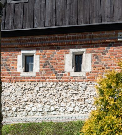 Zdjęcie nr 46: Kościół murowany z cegły, z użyciem zendrówki, na wysokim podmurowaniu z kamienia łupanego, jednonawowy, orientowany. 
Prezbiterium i nawa na planie prostokątów, nawa szersza i dłuższa od prezbiterium. Zakrystia na rzucie wydłużonego prostokąta przylega do wschodniej ściany prezbiterium, występując poza mury nawy. Prezbiterium od wschodu ujęte w narożach dwiema ukośnymi szkarpami, od południa jedną prostopadłą. Przy południowej ścianie nawy kruchta na planie kwadratu. Nawa w narożach ujęta szkarpami, od wschodu dwiema prostopadłymi, od zachodu ukośnymi. 
Prezbiterium dwuprzęsłowe, nakryte sklepieniem krzyżowo-żebrowym. Na zwornikach dwie tarcze z herbami Trzy Korony i Wieniawa. Zakrystia sklepiona kolebkowo. Nawa nakryta drewnianym stropem z kasetonami i rozetami. Kruchta sklepiona krzyżowo-żebrowo ze zwornikiem z tarczą z herbem Wieniawa. Otwór tęczowy w formie stojącego prostokąta zamkniętego łukiem ostrym. W zachodniej części nawy drewniany parapet chóru muzycznego wsparty na dwóch filarach. 
Fasada w jednej trzeciej wysokości odcięta kamiennym gzymsem kapnikowym, zakończona jodełkowym fryzem w partii muru, zwieńczona trójkątnym szczytem. Mur dekorowany zendrówką ułożoną „w zęby”, w partii szczytu w układzie rombowym. Na osi kamienny ostrołukowy portal o schodkowym nadprożu, dekorowanym krzyżującym się laskowaniem; węgary gładkie w jednej trzeciej wysokości przechodzące w piramidki i profilowanie powyżej. Nad portalem kamienna kwadratowa tablica, ujęta kamiennym obramieniem z tarczą z herbem Wieniawa. Ponad nią, na osi okulus w kamiennym obramieniu. 
Elewacje północna i południowa w części nawy w jednej trzeciej wysokości przedzielone kamiennym gzymsem kapnikowym, na zakończeniu ścian z gzymsem wieńczącym. Mur dekorowany zendrówką w układzie rombowym. Na elewacji południowej cztery okna w formie wydłużonego, stojącego prostokąta zamkniętego łukiem ostrym, w kamiennych obramieniach, podzielone laskowaniem. Południowa ściana prezbiterium zakończona gzymsem wieńczącym, w górnej części muru dekorowana zendrówką ułożoną „w zęby”. 
Szkarpy opinające nawę uskokowe, zwężające się ku górze, nakryte daszkami pulpitowymi. Szkarpy opinające prezbiterium nakryte daszkami pulpitowymi, podzielone gzymsami kapnikowymi. 
Kruchta od strony wschodniej i zachodniej podzielona kamiennym gzymsem kapnikowym, od południa zakończona gzymsem wieńczącym. Na ścianie południowej kruchty kamienny, ostrołukowy portal, o schodkowym nadprożu, dekorowanym krzyżującym się laskowaniem; węgary gładkie, w jednej trzeciej wysokości przechodzące w piramidki i profilowanie powyżej. Nad portalem kamienna tarcza z herbem Wieniawa. 
Elewacja wschodnia zwieńczona trójkątnym szczytem, w którego partii mur dekorowany jest zendrówką w układzie rombowym. Na osi okno w formie wydłużonego, stojącego prostokąta zamkniętego łukiem ostrym, w kamiennym obramieniu, zamurowane w trzech piątych wysokości, zakończone daszkiem pulpitowym. W dolnej części okna znajduje się ogrójec. 
Nawa i prezbiterium nakryte osobnymi blaszanymi dachami dwuspadowymi, kruchta i zakrystia pulpitowymi. Nad nawą blaszana wieżyczka na sygnaturkę z latarnią i hełmem baniastym.





