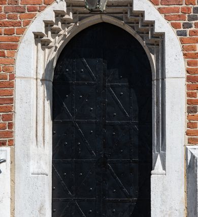 Zdjęcie nr 61: Kościół murowany z cegły, z użyciem zendrówki, na wysokim podmurowaniu z kamienia łupanego, jednonawowy, orientowany. 
Prezbiterium i nawa na planie prostokątów, nawa szersza i dłuższa od prezbiterium. Zakrystia na rzucie wydłużonego prostokąta przylega do wschodniej ściany prezbiterium, występując poza mury nawy. Prezbiterium od wschodu ujęte w narożach dwiema ukośnymi szkarpami, od południa jedną prostopadłą. Przy południowej ścianie nawy kruchta na planie kwadratu. Nawa w narożach ujęta szkarpami, od wschodu dwiema prostopadłymi, od zachodu ukośnymi. 
Prezbiterium dwuprzęsłowe, nakryte sklepieniem krzyżowo-żebrowym. Na zwornikach dwie tarcze z herbami Trzy Korony i Wieniawa. Zakrystia sklepiona kolebkowo. Nawa nakryta drewnianym stropem z kasetonami i rozetami. Kruchta sklepiona krzyżowo-żebrowo ze zwornikiem z tarczą z herbem Wieniawa. Otwór tęczowy w formie stojącego prostokąta zamkniętego łukiem ostrym. W zachodniej części nawy drewniany parapet chóru muzycznego wsparty na dwóch filarach. 
Fasada w jednej trzeciej wysokości odcięta kamiennym gzymsem kapnikowym, zakończona jodełkowym fryzem w partii muru, zwieńczona trójkątnym szczytem. Mur dekorowany zendrówką ułożoną „w zęby”, w partii szczytu w układzie rombowym. Na osi kamienny ostrołukowy portal o schodkowym nadprożu, dekorowanym krzyżującym się laskowaniem; węgary gładkie w jednej trzeciej wysokości przechodzące w piramidki i profilowanie powyżej. Nad portalem kamienna kwadratowa tablica, ujęta kamiennym obramieniem z tarczą z herbem Wieniawa. Ponad nią, na osi okulus w kamiennym obramieniu. 
Elewacje północna i południowa w części nawy w jednej trzeciej wysokości przedzielone kamiennym gzymsem kapnikowym, na zakończeniu ścian z gzymsem wieńczącym. Mur dekorowany zendrówką w układzie rombowym. Na elewacji południowej cztery okna w formie wydłużonego, stojącego prostokąta zamkniętego łukiem ostrym, w kamiennych obramieniach, podzielone laskowaniem. Południowa ściana prezbiterium zakończona gzymsem wieńczącym, w górnej części muru dekorowana zendrówką ułożoną „w zęby”. 
Szkarpy opinające nawę uskokowe, zwężające się ku górze, nakryte daszkami pulpitowymi. Szkarpy opinające prezbiterium nakryte daszkami pulpitowymi, podzielone gzymsami kapnikowymi. 
Kruchta od strony wschodniej i zachodniej podzielona kamiennym gzymsem kapnikowym, od południa zakończona gzymsem wieńczącym. Na ścianie południowej kruchty kamienny, ostrołukowy portal, o schodkowym nadprożu, dekorowanym krzyżującym się laskowaniem; węgary gładkie, w jednej trzeciej wysokości przechodzące w piramidki i profilowanie powyżej. Nad portalem kamienna tarcza z herbem Wieniawa. 
Elewacja wschodnia zwieńczona trójkątnym szczytem, w którego partii mur dekorowany jest zendrówką w układzie rombowym. Na osi okno w formie wydłużonego, stojącego prostokąta zamkniętego łukiem ostrym, w kamiennym obramieniu, zamurowane w trzech piątych wysokości, zakończone daszkiem pulpitowym. W dolnej części okna znajduje się ogrójec. 
Nawa i prezbiterium nakryte osobnymi blaszanymi dachami dwuspadowymi, kruchta i zakrystia pulpitowymi. Nad nawą blaszana wieżyczka na sygnaturkę z latarnią i hełmem baniastym.





