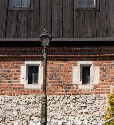 Zdjęcie nr 48: Kościół murowany z cegły, z użyciem zendrówki, na wysokim podmurowaniu z kamienia łupanego, jednonawowy, orientowany. 
Prezbiterium i nawa na planie prostokątów, nawa szersza i dłuższa od prezbiterium. Zakrystia na rzucie wydłużonego prostokąta przylega do wschodniej ściany prezbiterium, występując poza mury nawy. Prezbiterium od wschodu ujęte w narożach dwiema ukośnymi szkarpami, od południa jedną prostopadłą. Przy południowej ścianie nawy kruchta na planie kwadratu. Nawa w narożach ujęta szkarpami, od wschodu dwiema prostopadłymi, od zachodu ukośnymi. 
Prezbiterium dwuprzęsłowe, nakryte sklepieniem krzyżowo-żebrowym. Na zwornikach dwie tarcze z herbami Trzy Korony i Wieniawa. Zakrystia sklepiona kolebkowo. Nawa nakryta drewnianym stropem z kasetonami i rozetami. Kruchta sklepiona krzyżowo-żebrowo ze zwornikiem z tarczą z herbem Wieniawa. Otwór tęczowy w formie stojącego prostokąta zamkniętego łukiem ostrym. W zachodniej części nawy drewniany parapet chóru muzycznego wsparty na dwóch filarach. 
Fasada w jednej trzeciej wysokości odcięta kamiennym gzymsem kapnikowym, zakończona jodełkowym fryzem w partii muru, zwieńczona trójkątnym szczytem. Mur dekorowany zendrówką ułożoną „w zęby”, w partii szczytu w układzie rombowym. Na osi kamienny ostrołukowy portal o schodkowym nadprożu, dekorowanym krzyżującym się laskowaniem; węgary gładkie w jednej trzeciej wysokości przechodzące w piramidki i profilowanie powyżej. Nad portalem kamienna kwadratowa tablica, ujęta kamiennym obramieniem z tarczą z herbem Wieniawa. Ponad nią, na osi okulus w kamiennym obramieniu. 
Elewacje północna i południowa w części nawy w jednej trzeciej wysokości przedzielone kamiennym gzymsem kapnikowym, na zakończeniu ścian z gzymsem wieńczącym. Mur dekorowany zendrówką w układzie rombowym. Na elewacji południowej cztery okna w formie wydłużonego, stojącego prostokąta zamkniętego łukiem ostrym, w kamiennych obramieniach, podzielone laskowaniem. Południowa ściana prezbiterium zakończona gzymsem wieńczącym, w górnej części muru dekorowana zendrówką ułożoną „w zęby”. 
Szkarpy opinające nawę uskokowe, zwężające się ku górze, nakryte daszkami pulpitowymi. Szkarpy opinające prezbiterium nakryte daszkami pulpitowymi, podzielone gzymsami kapnikowymi. 
Kruchta od strony wschodniej i zachodniej podzielona kamiennym gzymsem kapnikowym, od południa zakończona gzymsem wieńczącym. Na ścianie południowej kruchty kamienny, ostrołukowy portal, o schodkowym nadprożu, dekorowanym krzyżującym się laskowaniem; węgary gładkie, w jednej trzeciej wysokości przechodzące w piramidki i profilowanie powyżej. Nad portalem kamienna tarcza z herbem Wieniawa. 
Elewacja wschodnia zwieńczona trójkątnym szczytem, w którego partii mur dekorowany jest zendrówką w układzie rombowym. Na osi okno w formie wydłużonego, stojącego prostokąta zamkniętego łukiem ostrym, w kamiennym obramieniu, zamurowane w trzech piątych wysokości, zakończone daszkiem pulpitowym. W dolnej części okna znajduje się ogrójec. 
Nawa i prezbiterium nakryte osobnymi blaszanymi dachami dwuspadowymi, kruchta i zakrystia pulpitowymi. Nad nawą blaszana wieżyczka na sygnaturkę z latarnią i hełmem baniastym.





