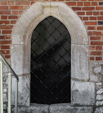 Zdjęcie nr 62: Kościół murowany z cegły, z użyciem zendrówki, na wysokim podmurowaniu z kamienia łupanego, jednonawowy, orientowany. 
Prezbiterium i nawa na planie prostokątów, nawa szersza i dłuższa od prezbiterium. Zakrystia na rzucie wydłużonego prostokąta przylega do wschodniej ściany prezbiterium, występując poza mury nawy. Prezbiterium od wschodu ujęte w narożach dwiema ukośnymi szkarpami, od południa jedną prostopadłą. Przy południowej ścianie nawy kruchta na planie kwadratu. Nawa w narożach ujęta szkarpami, od wschodu dwiema prostopadłymi, od zachodu ukośnymi. 
Prezbiterium dwuprzęsłowe, nakryte sklepieniem krzyżowo-żebrowym. Na zwornikach dwie tarcze z herbami Trzy Korony i Wieniawa. Zakrystia sklepiona kolebkowo. Nawa nakryta drewnianym stropem z kasetonami i rozetami. Kruchta sklepiona krzyżowo-żebrowo ze zwornikiem z tarczą z herbem Wieniawa. Otwór tęczowy w formie stojącego prostokąta zamkniętego łukiem ostrym. W zachodniej części nawy drewniany parapet chóru muzycznego wsparty na dwóch filarach. 
Fasada w jednej trzeciej wysokości odcięta kamiennym gzymsem kapnikowym, zakończona jodełkowym fryzem w partii muru, zwieńczona trójkątnym szczytem. Mur dekorowany zendrówką ułożoną „w zęby”, w partii szczytu w układzie rombowym. Na osi kamienny ostrołukowy portal o schodkowym nadprożu, dekorowanym krzyżującym się laskowaniem; węgary gładkie w jednej trzeciej wysokości przechodzące w piramidki i profilowanie powyżej. Nad portalem kamienna kwadratowa tablica, ujęta kamiennym obramieniem z tarczą z herbem Wieniawa. Ponad nią, na osi okulus w kamiennym obramieniu. 
Elewacje północna i południowa w części nawy w jednej trzeciej wysokości przedzielone kamiennym gzymsem kapnikowym, na zakończeniu ścian z gzymsem wieńczącym. Mur dekorowany zendrówką w układzie rombowym. Na elewacji południowej cztery okna w formie wydłużonego, stojącego prostokąta zamkniętego łukiem ostrym, w kamiennych obramieniach, podzielone laskowaniem. Południowa ściana prezbiterium zakończona gzymsem wieńczącym, w górnej części muru dekorowana zendrówką ułożoną „w zęby”. 
Szkarpy opinające nawę uskokowe, zwężające się ku górze, nakryte daszkami pulpitowymi. Szkarpy opinające prezbiterium nakryte daszkami pulpitowymi, podzielone gzymsami kapnikowymi. 
Kruchta od strony wschodniej i zachodniej podzielona kamiennym gzymsem kapnikowym, od południa zakończona gzymsem wieńczącym. Na ścianie południowej kruchty kamienny, ostrołukowy portal, o schodkowym nadprożu, dekorowanym krzyżującym się laskowaniem; węgary gładkie, w jednej trzeciej wysokości przechodzące w piramidki i profilowanie powyżej. Nad portalem kamienna tarcza z herbem Wieniawa. 
Elewacja wschodnia zwieńczona trójkątnym szczytem, w którego partii mur dekorowany jest zendrówką w układzie rombowym. Na osi okno w formie wydłużonego, stojącego prostokąta zamkniętego łukiem ostrym, w kamiennym obramieniu, zamurowane w trzech piątych wysokości, zakończone daszkiem pulpitowym. W dolnej części okna znajduje się ogrójec. 
Nawa i prezbiterium nakryte osobnymi blaszanymi dachami dwuspadowymi, kruchta i zakrystia pulpitowymi. Nad nawą blaszana wieżyczka na sygnaturkę z latarnią i hełmem baniastym.






