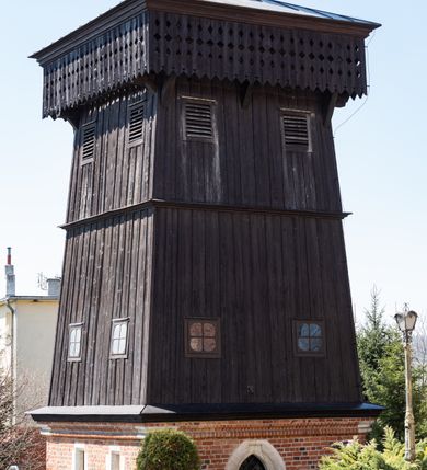 Zdjęcie nr 50: Kościół murowany z cegły, z użyciem zendrówki, na wysokim podmurowaniu z kamienia łupanego, jednonawowy, orientowany. 
Prezbiterium i nawa na planie prostokątów, nawa szersza i dłuższa od prezbiterium. Zakrystia na rzucie wydłużonego prostokąta przylega do wschodniej ściany prezbiterium, występując poza mury nawy. Prezbiterium od wschodu ujęte w narożach dwiema ukośnymi szkarpami, od południa jedną prostopadłą. Przy południowej ścianie nawy kruchta na planie kwadratu. Nawa w narożach ujęta szkarpami, od wschodu dwiema prostopadłymi, od zachodu ukośnymi. 
Prezbiterium dwuprzęsłowe, nakryte sklepieniem krzyżowo-żebrowym. Na zwornikach dwie tarcze z herbami Trzy Korony i Wieniawa. Zakrystia sklepiona kolebkowo. Nawa nakryta drewnianym stropem z kasetonami i rozetami. Kruchta sklepiona krzyżowo-żebrowo ze zwornikiem z tarczą z herbem Wieniawa. Otwór tęczowy w formie stojącego prostokąta zamkniętego łukiem ostrym. W zachodniej części nawy drewniany parapet chóru muzycznego wsparty na dwóch filarach. 
Fasada w jednej trzeciej wysokości odcięta kamiennym gzymsem kapnikowym, zakończona jodełkowym fryzem w partii muru, zwieńczona trójkątnym szczytem. Mur dekorowany zendrówką ułożoną „w zęby”, w partii szczytu w układzie rombowym. Na osi kamienny ostrołukowy portal o schodkowym nadprożu, dekorowanym krzyżującym się laskowaniem; węgary gładkie w jednej trzeciej wysokości przechodzące w piramidki i profilowanie powyżej. Nad portalem kamienna kwadratowa tablica, ujęta kamiennym obramieniem z tarczą z herbem Wieniawa. Ponad nią, na osi okulus w kamiennym obramieniu. 
Elewacje północna i południowa w części nawy w jednej trzeciej wysokości przedzielone kamiennym gzymsem kapnikowym, na zakończeniu ścian z gzymsem wieńczącym. Mur dekorowany zendrówką w układzie rombowym. Na elewacji południowej cztery okna w formie wydłużonego, stojącego prostokąta zamkniętego łukiem ostrym, w kamiennych obramieniach, podzielone laskowaniem. Południowa ściana prezbiterium zakończona gzymsem wieńczącym, w górnej części muru dekorowana zendrówką ułożoną „w zęby”. 
Szkarpy opinające nawę uskokowe, zwężające się ku górze, nakryte daszkami pulpitowymi. Szkarpy opinające prezbiterium nakryte daszkami pulpitowymi, podzielone gzymsami kapnikowymi. 
Kruchta od strony wschodniej i zachodniej podzielona kamiennym gzymsem kapnikowym, od południa zakończona gzymsem wieńczącym. Na ścianie południowej kruchty kamienny, ostrołukowy portal, o schodkowym nadprożu, dekorowanym krzyżującym się laskowaniem; węgary gładkie, w jednej trzeciej wysokości przechodzące w piramidki i profilowanie powyżej. Nad portalem kamienna tarcza z herbem Wieniawa. 
Elewacja wschodnia zwieńczona trójkątnym szczytem, w którego partii mur dekorowany jest zendrówką w układzie rombowym. Na osi okno w formie wydłużonego, stojącego prostokąta zamkniętego łukiem ostrym, w kamiennym obramieniu, zamurowane w trzech piątych wysokości, zakończone daszkiem pulpitowym. W dolnej części okna znajduje się ogrójec. 
Nawa i prezbiterium nakryte osobnymi blaszanymi dachami dwuspadowymi, kruchta i zakrystia pulpitowymi. Nad nawą blaszana wieżyczka na sygnaturkę z latarnią i hełmem baniastym.





