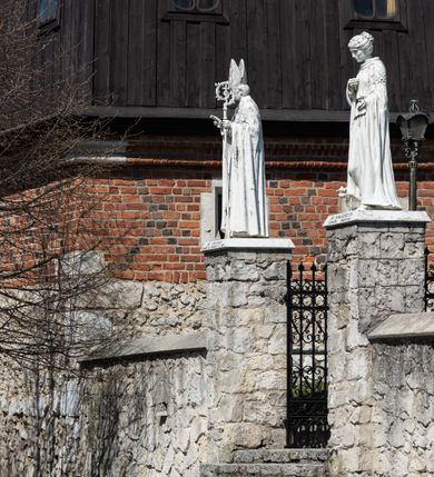 Zdjęcie nr 10: Kościół murowany z cegły, z użyciem zendrówki, na wysokim podmurowaniu z kamienia łupanego, jednonawowy, orientowany. 
Prezbiterium i nawa na planie prostokątów, nawa szersza i dłuższa od prezbiterium. Zakrystia na rzucie wydłużonego prostokąta przylega do wschodniej ściany prezbiterium, występując poza mury nawy. Prezbiterium od wschodu ujęte w narożach dwiema ukośnymi szkarpami, od południa jedną prostopadłą. Przy południowej ścianie nawy kruchta na planie kwadratu. Nawa w narożach ujęta szkarpami, od wschodu dwiema prostopadłymi, od zachodu ukośnymi. 
Prezbiterium dwuprzęsłowe, nakryte sklepieniem krzyżowo-żebrowym. Na zwornikach dwie tarcze z herbami Trzy Korony i Wieniawa. Zakrystia sklepiona kolebkowo. Nawa nakryta drewnianym stropem z kasetonami i rozetami. Kruchta sklepiona krzyżowo-żebrowo ze zwornikiem z tarczą z herbem Wieniawa. Otwór tęczowy w formie stojącego prostokąta zamkniętego łukiem ostrym. W zachodniej części nawy drewniany parapet chóru muzycznego wsparty na dwóch filarach. 
Fasada w jednej trzeciej wysokości odcięta kamiennym gzymsem kapnikowym, zakończona jodełkowym fryzem w partii muru, zwieńczona trójkątnym szczytem. Mur dekorowany zendrówką ułożoną „w zęby”, w partii szczytu w układzie rombowym. Na osi kamienny ostrołukowy portal o schodkowym nadprożu, dekorowanym krzyżującym się laskowaniem; węgary gładkie w jednej trzeciej wysokości przechodzące w piramidki i profilowanie powyżej. Nad portalem kamienna kwadratowa tablica, ujęta kamiennym obramieniem z tarczą z herbem Wieniawa. Ponad nią, na osi okulus w kamiennym obramieniu. 
Elewacje północna i południowa w części nawy w jednej trzeciej wysokości przedzielone kamiennym gzymsem kapnikowym, na zakończeniu ścian z gzymsem wieńczącym. Mur dekorowany zendrówką w układzie rombowym. Na elewacji południowej cztery okna w formie wydłużonego, stojącego prostokąta zamkniętego łukiem ostrym, w kamiennych obramieniach, podzielone laskowaniem. Południowa ściana prezbiterium zakończona gzymsem wieńczącym, w górnej części muru dekorowana zendrówką ułożoną „w zęby”. 
Szkarpy opinające nawę uskokowe, zwężające się ku górze, nakryte daszkami pulpitowymi. Szkarpy opinające prezbiterium nakryte daszkami pulpitowymi, podzielone gzymsami kapnikowymi. 
Kruchta od strony wschodniej i zachodniej podzielona kamiennym gzymsem kapnikowym, od południa zakończona gzymsem wieńczącym. Na ścianie południowej kruchty kamienny, ostrołukowy portal, o schodkowym nadprożu, dekorowanym krzyżującym się laskowaniem; węgary gładkie, w jednej trzeciej wysokości przechodzące w piramidki i profilowanie powyżej. Nad portalem kamienna tarcza z herbem Wieniawa. 
Elewacja wschodnia zwieńczona trójkątnym szczytem, w którego partii mur dekorowany jest zendrówką w układzie rombowym. Na osi okno w formie wydłużonego, stojącego prostokąta zamkniętego łukiem ostrym, w kamiennym obramieniu, zamurowane w trzech piątych wysokości, zakończone daszkiem pulpitowym. W dolnej części okna znajduje się ogrójec. 
Nawa i prezbiterium nakryte osobnymi blaszanymi dachami dwuspadowymi, kruchta i zakrystia pulpitowymi. Nad nawą blaszana wieżyczka na sygnaturkę z latarnią i hełmem baniastym.





