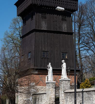 Zdjęcie nr 8: Kościół murowany z cegły, z użyciem zendrówki, na wysokim podmurowaniu z kamienia łupanego, jednonawowy, orientowany. 
Prezbiterium i nawa na planie prostokątów, nawa szersza i dłuższa od prezbiterium. Zakrystia na rzucie wydłużonego prostokąta przylega do wschodniej ściany prezbiterium, występując poza mury nawy. Prezbiterium od wschodu ujęte w narożach dwiema ukośnymi szkarpami, od południa jedną prostopadłą. Przy południowej ścianie nawy kruchta na planie kwadratu. Nawa w narożach ujęta szkarpami, od wschodu dwiema prostopadłymi, od zachodu ukośnymi. 
Prezbiterium dwuprzęsłowe, nakryte sklepieniem krzyżowo-żebrowym. Na zwornikach dwie tarcze z herbami Trzy Korony i Wieniawa. Zakrystia sklepiona kolebkowo. Nawa nakryta drewnianym stropem z kasetonami i rozetami. Kruchta sklepiona krzyżowo-żebrowo ze zwornikiem z tarczą z herbem Wieniawa. Otwór tęczowy w formie stojącego prostokąta zamkniętego łukiem ostrym. W zachodniej części nawy drewniany parapet chóru muzycznego wsparty na dwóch filarach. 
Fasada w jednej trzeciej wysokości odcięta kamiennym gzymsem kapnikowym, zakończona jodełkowym fryzem w partii muru, zwieńczona trójkątnym szczytem. Mur dekorowany zendrówką ułożoną „w zęby”, w partii szczytu w układzie rombowym. Na osi kamienny ostrołukowy portal o schodkowym nadprożu, dekorowanym krzyżującym się laskowaniem; węgary gładkie w jednej trzeciej wysokości przechodzące w piramidki i profilowanie powyżej. Nad portalem kamienna kwadratowa tablica, ujęta kamiennym obramieniem z tarczą z herbem Wieniawa. Ponad nią, na osi okulus w kamiennym obramieniu. 
Elewacje północna i południowa w części nawy w jednej trzeciej wysokości przedzielone kamiennym gzymsem kapnikowym, na zakończeniu ścian z gzymsem wieńczącym. Mur dekorowany zendrówką w układzie rombowym. Na elewacji południowej cztery okna w formie wydłużonego, stojącego prostokąta zamkniętego łukiem ostrym, w kamiennych obramieniach, podzielone laskowaniem. Południowa ściana prezbiterium zakończona gzymsem wieńczącym, w górnej części muru dekorowana zendrówką ułożoną „w zęby”. 
Szkarpy opinające nawę uskokowe, zwężające się ku górze, nakryte daszkami pulpitowymi. Szkarpy opinające prezbiterium nakryte daszkami pulpitowymi, podzielone gzymsami kapnikowymi. 
Kruchta od strony wschodniej i zachodniej podzielona kamiennym gzymsem kapnikowym, od południa zakończona gzymsem wieńczącym. Na ścianie południowej kruchty kamienny, ostrołukowy portal, o schodkowym nadprożu, dekorowanym krzyżującym się laskowaniem; węgary gładkie, w jednej trzeciej wysokości przechodzące w piramidki i profilowanie powyżej. Nad portalem kamienna tarcza z herbem Wieniawa. 
Elewacja wschodnia zwieńczona trójkątnym szczytem, w którego partii mur dekorowany jest zendrówką w układzie rombowym. Na osi okno w formie wydłużonego, stojącego prostokąta zamkniętego łukiem ostrym, w kamiennym obramieniu, zamurowane w trzech piątych wysokości, zakończone daszkiem pulpitowym. W dolnej części okna znajduje się ogrójec. 
Nawa i prezbiterium nakryte osobnymi blaszanymi dachami dwuspadowymi, kruchta i zakrystia pulpitowymi. Nad nawą blaszana wieżyczka na sygnaturkę z latarnią i hełmem baniastym.






