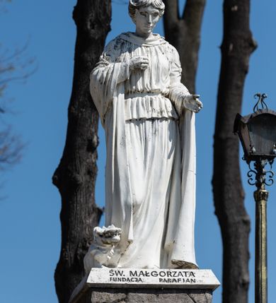 Zdjęcie nr 19: Kościół murowany z cegły, z użyciem zendrówki, na wysokim podmurowaniu z kamienia łupanego, jednonawowy, orientowany. 
Prezbiterium i nawa na planie prostokątów, nawa szersza i dłuższa od prezbiterium. Zakrystia na rzucie wydłużonego prostokąta przylega do wschodniej ściany prezbiterium, występując poza mury nawy. Prezbiterium od wschodu ujęte w narożach dwiema ukośnymi szkarpami, od południa jedną prostopadłą. Przy południowej ścianie nawy kruchta na planie kwadratu. Nawa w narożach ujęta szkarpami, od wschodu dwiema prostopadłymi, od zachodu ukośnymi. 
Prezbiterium dwuprzęsłowe, nakryte sklepieniem krzyżowo-żebrowym. Na zwornikach dwie tarcze z herbami Trzy Korony i Wieniawa. Zakrystia sklepiona kolebkowo. Nawa nakryta drewnianym stropem z kasetonami i rozetami. Kruchta sklepiona krzyżowo-żebrowo ze zwornikiem z tarczą z herbem Wieniawa. Otwór tęczowy w formie stojącego prostokąta zamkniętego łukiem ostrym. W zachodniej części nawy drewniany parapet chóru muzycznego wsparty na dwóch filarach. 
Fasada w jednej trzeciej wysokości odcięta kamiennym gzymsem kapnikowym, zakończona jodełkowym fryzem w partii muru, zwieńczona trójkątnym szczytem. Mur dekorowany zendrówką ułożoną „w zęby”, w partii szczytu w układzie rombowym. Na osi kamienny ostrołukowy portal o schodkowym nadprożu, dekorowanym krzyżującym się laskowaniem; węgary gładkie w jednej trzeciej wysokości przechodzące w piramidki i profilowanie powyżej. Nad portalem kamienna kwadratowa tablica, ujęta kamiennym obramieniem z tarczą z herbem Wieniawa. Ponad nią, na osi okulus w kamiennym obramieniu. 
Elewacje północna i południowa w części nawy w jednej trzeciej wysokości przedzielone kamiennym gzymsem kapnikowym, na zakończeniu ścian z gzymsem wieńczącym. Mur dekorowany zendrówką w układzie rombowym. Na elewacji południowej cztery okna w formie wydłużonego, stojącego prostokąta zamkniętego łukiem ostrym, w kamiennych obramieniach, podzielone laskowaniem. Południowa ściana prezbiterium zakończona gzymsem wieńczącym, w górnej części muru dekorowana zendrówką ułożoną „w zęby”. 
Szkarpy opinające nawę uskokowe, zwężające się ku górze, nakryte daszkami pulpitowymi. Szkarpy opinające prezbiterium nakryte daszkami pulpitowymi, podzielone gzymsami kapnikowymi. 
Kruchta od strony wschodniej i zachodniej podzielona kamiennym gzymsem kapnikowym, od południa zakończona gzymsem wieńczącym. Na ścianie południowej kruchty kamienny, ostrołukowy portal, o schodkowym nadprożu, dekorowanym krzyżującym się laskowaniem; węgary gładkie, w jednej trzeciej wysokości przechodzące w piramidki i profilowanie powyżej. Nad portalem kamienna tarcza z herbem Wieniawa. 
Elewacja wschodnia zwieńczona trójkątnym szczytem, w którego partii mur dekorowany jest zendrówką w układzie rombowym. Na osi okno w formie wydłużonego, stojącego prostokąta zamkniętego łukiem ostrym, w kamiennym obramieniu, zamurowane w trzech piątych wysokości, zakończone daszkiem pulpitowym. W dolnej części okna znajduje się ogrójec. 
Nawa i prezbiterium nakryte osobnymi blaszanymi dachami dwuspadowymi, kruchta i zakrystia pulpitowymi. Nad nawą blaszana wieżyczka na sygnaturkę z latarnią i hełmem baniastym.





