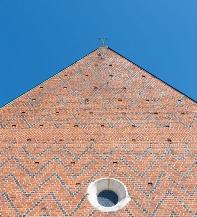 Zdjęcie nr 78: Kościół murowany z cegły, z użyciem zendrówki, na wysokim podmurowaniu z kamienia łupanego, jednonawowy, orientowany. 
Prezbiterium i nawa na planie prostokątów, nawa szersza i dłuższa od prezbiterium. Zakrystia na rzucie wydłużonego prostokąta przylega do wschodniej ściany prezbiterium, występując poza mury nawy. Prezbiterium od wschodu ujęte w narożach dwiema ukośnymi szkarpami, od południa jedną prostopadłą. Przy południowej ścianie nawy kruchta na planie kwadratu. Nawa w narożach ujęta szkarpami, od wschodu dwiema prostopadłymi, od zachodu ukośnymi. 
Prezbiterium dwuprzęsłowe, nakryte sklepieniem krzyżowo-żebrowym. Na zwornikach dwie tarcze z herbami Trzy Korony i Wieniawa. Zakrystia sklepiona kolebkowo. Nawa nakryta drewnianym stropem z kasetonami i rozetami. Kruchta sklepiona krzyżowo-żebrowo ze zwornikiem z tarczą z herbem Wieniawa. Otwór tęczowy w formie stojącego prostokąta zamkniętego łukiem ostrym. W zachodniej części nawy drewniany parapet chóru muzycznego wsparty na dwóch filarach. 
Fasada w jednej trzeciej wysokości odcięta kamiennym gzymsem kapnikowym, zakończona jodełkowym fryzem w partii muru, zwieńczona trójkątnym szczytem. Mur dekorowany zendrówką ułożoną „w zęby”, w partii szczytu w układzie rombowym. Na osi kamienny ostrołukowy portal o schodkowym nadprożu, dekorowanym krzyżującym się laskowaniem; węgary gładkie w jednej trzeciej wysokości przechodzące w piramidki i profilowanie powyżej. Nad portalem kamienna kwadratowa tablica, ujęta kamiennym obramieniem z tarczą z herbem Wieniawa. Ponad nią, na osi okulus w kamiennym obramieniu. 
Elewacje północna i południowa w części nawy w jednej trzeciej wysokości przedzielone kamiennym gzymsem kapnikowym, na zakończeniu ścian z gzymsem wieńczącym. Mur dekorowany zendrówką w układzie rombowym. Na elewacji południowej cztery okna w formie wydłużonego, stojącego prostokąta zamkniętego łukiem ostrym, w kamiennych obramieniach, podzielone laskowaniem. Południowa ściana prezbiterium zakończona gzymsem wieńczącym, w górnej części muru dekorowana zendrówką ułożoną „w zęby”. 
Szkarpy opinające nawę uskokowe, zwężające się ku górze, nakryte daszkami pulpitowymi. Szkarpy opinające prezbiterium nakryte daszkami pulpitowymi, podzielone gzymsami kapnikowymi. 
Kruchta od strony wschodniej i zachodniej podzielona kamiennym gzymsem kapnikowym, od południa zakończona gzymsem wieńczącym. Na ścianie południowej kruchty kamienny, ostrołukowy portal, o schodkowym nadprożu, dekorowanym krzyżującym się laskowaniem; węgary gładkie, w jednej trzeciej wysokości przechodzące w piramidki i profilowanie powyżej. Nad portalem kamienna tarcza z herbem Wieniawa. 
Elewacja wschodnia zwieńczona trójkątnym szczytem, w którego partii mur dekorowany jest zendrówką w układzie rombowym. Na osi okno w formie wydłużonego, stojącego prostokąta zamkniętego łukiem ostrym, w kamiennym obramieniu, zamurowane w trzech piątych wysokości, zakończone daszkiem pulpitowym. W dolnej części okna znajduje się ogrójec. 
Nawa i prezbiterium nakryte osobnymi blaszanymi dachami dwuspadowymi, kruchta i zakrystia pulpitowymi. Nad nawą blaszana wieżyczka na sygnaturkę z latarnią i hełmem baniastym.





