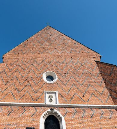 Zdjęcie nr 79: Kościół murowany z cegły, z użyciem zendrówki, na wysokim podmurowaniu z kamienia łupanego, jednonawowy, orientowany. 
Prezbiterium i nawa na planie prostokątów, nawa szersza i dłuższa od prezbiterium. Zakrystia na rzucie wydłużonego prostokąta przylega do wschodniej ściany prezbiterium, występując poza mury nawy. Prezbiterium od wschodu ujęte w narożach dwiema ukośnymi szkarpami, od południa jedną prostopadłą. Przy południowej ścianie nawy kruchta na planie kwadratu. Nawa w narożach ujęta szkarpami, od wschodu dwiema prostopadłymi, od zachodu ukośnymi. 
Prezbiterium dwuprzęsłowe, nakryte sklepieniem krzyżowo-żebrowym. Na zwornikach dwie tarcze z herbami Trzy Korony i Wieniawa. Zakrystia sklepiona kolebkowo. Nawa nakryta drewnianym stropem z kasetonami i rozetami. Kruchta sklepiona krzyżowo-żebrowo ze zwornikiem z tarczą z herbem Wieniawa. Otwór tęczowy w formie stojącego prostokąta zamkniętego łukiem ostrym. W zachodniej części nawy drewniany parapet chóru muzycznego wsparty na dwóch filarach. 
Fasada w jednej trzeciej wysokości odcięta kamiennym gzymsem kapnikowym, zakończona jodełkowym fryzem w partii muru, zwieńczona trójkątnym szczytem. Mur dekorowany zendrówką ułożoną „w zęby”, w partii szczytu w układzie rombowym. Na osi kamienny ostrołukowy portal o schodkowym nadprożu, dekorowanym krzyżującym się laskowaniem; węgary gładkie w jednej trzeciej wysokości przechodzące w piramidki i profilowanie powyżej. Nad portalem kamienna kwadratowa tablica, ujęta kamiennym obramieniem z tarczą z herbem Wieniawa. Ponad nią, na osi okulus w kamiennym obramieniu. 
Elewacje północna i południowa w części nawy w jednej trzeciej wysokości przedzielone kamiennym gzymsem kapnikowym, na zakończeniu ścian z gzymsem wieńczącym. Mur dekorowany zendrówką w układzie rombowym. Na elewacji południowej cztery okna w formie wydłużonego, stojącego prostokąta zamkniętego łukiem ostrym, w kamiennych obramieniach, podzielone laskowaniem. Południowa ściana prezbiterium zakończona gzymsem wieńczącym, w górnej części muru dekorowana zendrówką ułożoną „w zęby”. 
Szkarpy opinające nawę uskokowe, zwężające się ku górze, nakryte daszkami pulpitowymi. Szkarpy opinające prezbiterium nakryte daszkami pulpitowymi, podzielone gzymsami kapnikowymi. 
Kruchta od strony wschodniej i zachodniej podzielona kamiennym gzymsem kapnikowym, od południa zakończona gzymsem wieńczącym. Na ścianie południowej kruchty kamienny, ostrołukowy portal, o schodkowym nadprożu, dekorowanym krzyżującym się laskowaniem; węgary gładkie, w jednej trzeciej wysokości przechodzące w piramidki i profilowanie powyżej. Nad portalem kamienna tarcza z herbem Wieniawa. 
Elewacja wschodnia zwieńczona trójkątnym szczytem, w którego partii mur dekorowany jest zendrówką w układzie rombowym. Na osi okno w formie wydłużonego, stojącego prostokąta zamkniętego łukiem ostrym, w kamiennym obramieniu, zamurowane w trzech piątych wysokości, zakończone daszkiem pulpitowym. W dolnej części okna znajduje się ogrójec. 
Nawa i prezbiterium nakryte osobnymi blaszanymi dachami dwuspadowymi, kruchta i zakrystia pulpitowymi. Nad nawą blaszana wieżyczka na sygnaturkę z latarnią i hełmem baniastym.





