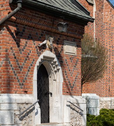 Zdjęcie nr 81: Kościół murowany z cegły, z użyciem zendrówki, na wysokim podmurowaniu z kamienia łupanego, jednonawowy, orientowany. 
Prezbiterium i nawa na planie prostokątów, nawa szersza i dłuższa od prezbiterium. Zakrystia na rzucie wydłużonego prostokąta przylega do wschodniej ściany prezbiterium, występując poza mury nawy. Prezbiterium od wschodu ujęte w narożach dwiema ukośnymi szkarpami, od południa jedną prostopadłą. Przy południowej ścianie nawy kruchta na planie kwadratu. Nawa w narożach ujęta szkarpami, od wschodu dwiema prostopadłymi, od zachodu ukośnymi. 
Prezbiterium dwuprzęsłowe, nakryte sklepieniem krzyżowo-żebrowym. Na zwornikach dwie tarcze z herbami Trzy Korony i Wieniawa. Zakrystia sklepiona kolebkowo. Nawa nakryta drewnianym stropem z kasetonami i rozetami. Kruchta sklepiona krzyżowo-żebrowo ze zwornikiem z tarczą z herbem Wieniawa. Otwór tęczowy w formie stojącego prostokąta zamkniętego łukiem ostrym. W zachodniej części nawy drewniany parapet chóru muzycznego wsparty na dwóch filarach. 
Fasada w jednej trzeciej wysokości odcięta kamiennym gzymsem kapnikowym, zakończona jodełkowym fryzem w partii muru, zwieńczona trójkątnym szczytem. Mur dekorowany zendrówką ułożoną „w zęby”, w partii szczytu w układzie rombowym. Na osi kamienny ostrołukowy portal o schodkowym nadprożu, dekorowanym krzyżującym się laskowaniem; węgary gładkie w jednej trzeciej wysokości przechodzące w piramidki i profilowanie powyżej. Nad portalem kamienna kwadratowa tablica, ujęta kamiennym obramieniem z tarczą z herbem Wieniawa. Ponad nią, na osi okulus w kamiennym obramieniu. 
Elewacje północna i południowa w części nawy w jednej trzeciej wysokości przedzielone kamiennym gzymsem kapnikowym, na zakończeniu ścian z gzymsem wieńczącym. Mur dekorowany zendrówką w układzie rombowym. Na elewacji południowej cztery okna w formie wydłużonego, stojącego prostokąta zamkniętego łukiem ostrym, w kamiennych obramieniach, podzielone laskowaniem. Południowa ściana prezbiterium zakończona gzymsem wieńczącym, w górnej części muru dekorowana zendrówką ułożoną „w zęby”. 
Szkarpy opinające nawę uskokowe, zwężające się ku górze, nakryte daszkami pulpitowymi. Szkarpy opinające prezbiterium nakryte daszkami pulpitowymi, podzielone gzymsami kapnikowymi. 
Kruchta od strony wschodniej i zachodniej podzielona kamiennym gzymsem kapnikowym, od południa zakończona gzymsem wieńczącym. Na ścianie południowej kruchty kamienny, ostrołukowy portal, o schodkowym nadprożu, dekorowanym krzyżującym się laskowaniem; węgary gładkie, w jednej trzeciej wysokości przechodzące w piramidki i profilowanie powyżej. Nad portalem kamienna tarcza z herbem Wieniawa. 
Elewacja wschodnia zwieńczona trójkątnym szczytem, w którego partii mur dekorowany jest zendrówką w układzie rombowym. Na osi okno w formie wydłużonego, stojącego prostokąta zamkniętego łukiem ostrym, w kamiennym obramieniu, zamurowane w trzech piątych wysokości, zakończone daszkiem pulpitowym. W dolnej części okna znajduje się ogrójec. 
Nawa i prezbiterium nakryte osobnymi blaszanymi dachami dwuspadowymi, kruchta i zakrystia pulpitowymi. Nad nawą blaszana wieżyczka na sygnaturkę z latarnią i hełmem baniastym.





