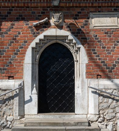 Zdjęcie nr 82: Kościół murowany z cegły, z użyciem zendrówki, na wysokim podmurowaniu z kamienia łupanego, jednonawowy, orientowany. 
Prezbiterium i nawa na planie prostokątów, nawa szersza i dłuższa od prezbiterium. Zakrystia na rzucie wydłużonego prostokąta przylega do wschodniej ściany prezbiterium, występując poza mury nawy. Prezbiterium od wschodu ujęte w narożach dwiema ukośnymi szkarpami, od południa jedną prostopadłą. Przy południowej ścianie nawy kruchta na planie kwadratu. Nawa w narożach ujęta szkarpami, od wschodu dwiema prostopadłymi, od zachodu ukośnymi. 
Prezbiterium dwuprzęsłowe, nakryte sklepieniem krzyżowo-żebrowym. Na zwornikach dwie tarcze z herbami Trzy Korony i Wieniawa. Zakrystia sklepiona kolebkowo. Nawa nakryta drewnianym stropem z kasetonami i rozetami. Kruchta sklepiona krzyżowo-żebrowo ze zwornikiem z tarczą z herbem Wieniawa. Otwór tęczowy w formie stojącego prostokąta zamkniętego łukiem ostrym. W zachodniej części nawy drewniany parapet chóru muzycznego wsparty na dwóch filarach. 
Fasada w jednej trzeciej wysokości odcięta kamiennym gzymsem kapnikowym, zakończona jodełkowym fryzem w partii muru, zwieńczona trójkątnym szczytem. Mur dekorowany zendrówką ułożoną „w zęby”, w partii szczytu w układzie rombowym. Na osi kamienny ostrołukowy portal o schodkowym nadprożu, dekorowanym krzyżującym się laskowaniem; węgary gładkie w jednej trzeciej wysokości przechodzące w piramidki i profilowanie powyżej. Nad portalem kamienna kwadratowa tablica, ujęta kamiennym obramieniem z tarczą z herbem Wieniawa. Ponad nią, na osi okulus w kamiennym obramieniu. 
Elewacje północna i południowa w części nawy w jednej trzeciej wysokości przedzielone kamiennym gzymsem kapnikowym, na zakończeniu ścian z gzymsem wieńczącym. Mur dekorowany zendrówką w układzie rombowym. Na elewacji południowej cztery okna w formie wydłużonego, stojącego prostokąta zamkniętego łukiem ostrym, w kamiennych obramieniach, podzielone laskowaniem. Południowa ściana prezbiterium zakończona gzymsem wieńczącym, w górnej części muru dekorowana zendrówką ułożoną „w zęby”. 
Szkarpy opinające nawę uskokowe, zwężające się ku górze, nakryte daszkami pulpitowymi. Szkarpy opinające prezbiterium nakryte daszkami pulpitowymi, podzielone gzymsami kapnikowymi. 
Kruchta od strony wschodniej i zachodniej podzielona kamiennym gzymsem kapnikowym, od południa zakończona gzymsem wieńczącym. Na ścianie południowej kruchty kamienny, ostrołukowy portal, o schodkowym nadprożu, dekorowanym krzyżującym się laskowaniem; węgary gładkie, w jednej trzeciej wysokości przechodzące w piramidki i profilowanie powyżej. Nad portalem kamienna tarcza z herbem Wieniawa. 
Elewacja wschodnia zwieńczona trójkątnym szczytem, w którego partii mur dekorowany jest zendrówką w układzie rombowym. Na osi okno w formie wydłużonego, stojącego prostokąta zamkniętego łukiem ostrym, w kamiennym obramieniu, zamurowane w trzech piątych wysokości, zakończone daszkiem pulpitowym. W dolnej części okna znajduje się ogrójec. 
Nawa i prezbiterium nakryte osobnymi blaszanymi dachami dwuspadowymi, kruchta i zakrystia pulpitowymi. Nad nawą blaszana wieżyczka na sygnaturkę z latarnią i hełmem baniastym.





