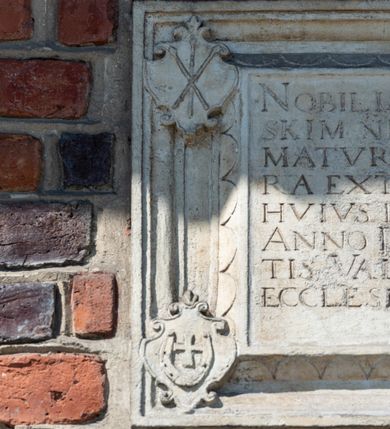 Zdjęcie nr 101: Kościół murowany z cegły, z użyciem zendrówki, na wysokim podmurowaniu z kamienia łupanego, jednonawowy, orientowany. 
Prezbiterium i nawa na planie prostokątów, nawa szersza i dłuższa od prezbiterium. Zakrystia na rzucie wydłużonego prostokąta przylega do wschodniej ściany prezbiterium, występując poza mury nawy. Prezbiterium od wschodu ujęte w narożach dwiema ukośnymi szkarpami, od południa jedną prostopadłą. Przy południowej ścianie nawy kruchta na planie kwadratu. Nawa w narożach ujęta szkarpami, od wschodu dwiema prostopadłymi, od zachodu ukośnymi. 
Prezbiterium dwuprzęsłowe, nakryte sklepieniem krzyżowo-żebrowym. Na zwornikach dwie tarcze z herbami Trzy Korony i Wieniawa. Zakrystia sklepiona kolebkowo. Nawa nakryta drewnianym stropem z kasetonami i rozetami. Kruchta sklepiona krzyżowo-żebrowo ze zwornikiem z tarczą z herbem Wieniawa. Otwór tęczowy w formie stojącego prostokąta zamkniętego łukiem ostrym. W zachodniej części nawy drewniany parapet chóru muzycznego wsparty na dwóch filarach. 
Fasada w jednej trzeciej wysokości odcięta kamiennym gzymsem kapnikowym, zakończona jodełkowym fryzem w partii muru, zwieńczona trójkątnym szczytem. Mur dekorowany zendrówką ułożoną „w zęby”, w partii szczytu w układzie rombowym. Na osi kamienny ostrołukowy portal o schodkowym nadprożu, dekorowanym krzyżującym się laskowaniem; węgary gładkie w jednej trzeciej wysokości przechodzące w piramidki i profilowanie powyżej. Nad portalem kamienna kwadratowa tablica, ujęta kamiennym obramieniem z tarczą z herbem Wieniawa. Ponad nią, na osi okulus w kamiennym obramieniu. 
Elewacje północna i południowa w części nawy w jednej trzeciej wysokości przedzielone kamiennym gzymsem kapnikowym, na zakończeniu ścian z gzymsem wieńczącym. Mur dekorowany zendrówką w układzie rombowym. Na elewacji południowej cztery okna w formie wydłużonego, stojącego prostokąta zamkniętego łukiem ostrym, w kamiennych obramieniach, podzielone laskowaniem. Południowa ściana prezbiterium zakończona gzymsem wieńczącym, w górnej części muru dekorowana zendrówką ułożoną „w zęby”. 
Szkarpy opinające nawę uskokowe, zwężające się ku górze, nakryte daszkami pulpitowymi. Szkarpy opinające prezbiterium nakryte daszkami pulpitowymi, podzielone gzymsami kapnikowymi. 
Kruchta od strony wschodniej i zachodniej podzielona kamiennym gzymsem kapnikowym, od południa zakończona gzymsem wieńczącym. Na ścianie południowej kruchty kamienny, ostrołukowy portal, o schodkowym nadprożu, dekorowanym krzyżującym się laskowaniem; węgary gładkie, w jednej trzeciej wysokości przechodzące w piramidki i profilowanie powyżej. Nad portalem kamienna tarcza z herbem Wieniawa. 
Elewacja wschodnia zwieńczona trójkątnym szczytem, w którego partii mur dekorowany jest zendrówką w układzie rombowym. Na osi okno w formie wydłużonego, stojącego prostokąta zamkniętego łukiem ostrym, w kamiennym obramieniu, zamurowane w trzech piątych wysokości, zakończone daszkiem pulpitowym. W dolnej części okna znajduje się ogrójec. 
Nawa i prezbiterium nakryte osobnymi blaszanymi dachami dwuspadowymi, kruchta i zakrystia pulpitowymi. Nad nawą blaszana wieżyczka na sygnaturkę z latarnią i hełmem baniastym.





