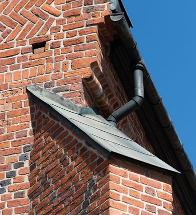 Zdjęcie nr 87: Kościół murowany z cegły, z użyciem zendrówki, na wysokim podmurowaniu z kamienia łupanego, jednonawowy, orientowany. 
Prezbiterium i nawa na planie prostokątów, nawa szersza i dłuższa od prezbiterium. Zakrystia na rzucie wydłużonego prostokąta przylega do wschodniej ściany prezbiterium, występując poza mury nawy. Prezbiterium od wschodu ujęte w narożach dwiema ukośnymi szkarpami, od południa jedną prostopadłą. Przy południowej ścianie nawy kruchta na planie kwadratu. Nawa w narożach ujęta szkarpami, od wschodu dwiema prostopadłymi, od zachodu ukośnymi. 
Prezbiterium dwuprzęsłowe, nakryte sklepieniem krzyżowo-żebrowym. Na zwornikach dwie tarcze z herbami Trzy Korony i Wieniawa. Zakrystia sklepiona kolebkowo. Nawa nakryta drewnianym stropem z kasetonami i rozetami. Kruchta sklepiona krzyżowo-żebrowo ze zwornikiem z tarczą z herbem Wieniawa. Otwór tęczowy w formie stojącego prostokąta zamkniętego łukiem ostrym. W zachodniej części nawy drewniany parapet chóru muzycznego wsparty na dwóch filarach. 
Fasada w jednej trzeciej wysokości odcięta kamiennym gzymsem kapnikowym, zakończona jodełkowym fryzem w partii muru, zwieńczona trójkątnym szczytem. Mur dekorowany zendrówką ułożoną „w zęby”, w partii szczytu w układzie rombowym. Na osi kamienny ostrołukowy portal o schodkowym nadprożu, dekorowanym krzyżującym się laskowaniem; węgary gładkie w jednej trzeciej wysokości przechodzące w piramidki i profilowanie powyżej. Nad portalem kamienna kwadratowa tablica, ujęta kamiennym obramieniem z tarczą z herbem Wieniawa. Ponad nią, na osi okulus w kamiennym obramieniu. 
Elewacje północna i południowa w części nawy w jednej trzeciej wysokości przedzielone kamiennym gzymsem kapnikowym, na zakończeniu ścian z gzymsem wieńczącym. Mur dekorowany zendrówką w układzie rombowym. Na elewacji południowej cztery okna w formie wydłużonego, stojącego prostokąta zamkniętego łukiem ostrym, w kamiennych obramieniach, podzielone laskowaniem. Południowa ściana prezbiterium zakończona gzymsem wieńczącym, w górnej części muru dekorowana zendrówką ułożoną „w zęby”. 
Szkarpy opinające nawę uskokowe, zwężające się ku górze, nakryte daszkami pulpitowymi. Szkarpy opinające prezbiterium nakryte daszkami pulpitowymi, podzielone gzymsami kapnikowymi. 
Kruchta od strony wschodniej i zachodniej podzielona kamiennym gzymsem kapnikowym, od południa zakończona gzymsem wieńczącym. Na ścianie południowej kruchty kamienny, ostrołukowy portal, o schodkowym nadprożu, dekorowanym krzyżującym się laskowaniem; węgary gładkie, w jednej trzeciej wysokości przechodzące w piramidki i profilowanie powyżej. Nad portalem kamienna tarcza z herbem Wieniawa. 
Elewacja wschodnia zwieńczona trójkątnym szczytem, w którego partii mur dekorowany jest zendrówką w układzie rombowym. Na osi okno w formie wydłużonego, stojącego prostokąta zamkniętego łukiem ostrym, w kamiennym obramieniu, zamurowane w trzech piątych wysokości, zakończone daszkiem pulpitowym. W dolnej części okna znajduje się ogrójec. 
Nawa i prezbiterium nakryte osobnymi blaszanymi dachami dwuspadowymi, kruchta i zakrystia pulpitowymi. Nad nawą blaszana wieżyczka na sygnaturkę z latarnią i hełmem baniastym.





