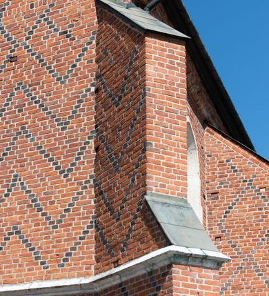 Zdjęcie nr 88: Kościół murowany z cegły, z użyciem zendrówki, na wysokim podmurowaniu z kamienia łupanego, jednonawowy, orientowany. 
Prezbiterium i nawa na planie prostokątów, nawa szersza i dłuższa od prezbiterium. Zakrystia na rzucie wydłużonego prostokąta przylega do wschodniej ściany prezbiterium, występując poza mury nawy. Prezbiterium od wschodu ujęte w narożach dwiema ukośnymi szkarpami, od południa jedną prostopadłą. Przy południowej ścianie nawy kruchta na planie kwadratu. Nawa w narożach ujęta szkarpami, od wschodu dwiema prostopadłymi, od zachodu ukośnymi. 
Prezbiterium dwuprzęsłowe, nakryte sklepieniem krzyżowo-żebrowym. Na zwornikach dwie tarcze z herbami Trzy Korony i Wieniawa. Zakrystia sklepiona kolebkowo. Nawa nakryta drewnianym stropem z kasetonami i rozetami. Kruchta sklepiona krzyżowo-żebrowo ze zwornikiem z tarczą z herbem Wieniawa. Otwór tęczowy w formie stojącego prostokąta zamkniętego łukiem ostrym. W zachodniej części nawy drewniany parapet chóru muzycznego wsparty na dwóch filarach. 
Fasada w jednej trzeciej wysokości odcięta kamiennym gzymsem kapnikowym, zakończona jodełkowym fryzem w partii muru, zwieńczona trójkątnym szczytem. Mur dekorowany zendrówką ułożoną „w zęby”, w partii szczytu w układzie rombowym. Na osi kamienny ostrołukowy portal o schodkowym nadprożu, dekorowanym krzyżującym się laskowaniem; węgary gładkie w jednej trzeciej wysokości przechodzące w piramidki i profilowanie powyżej. Nad portalem kamienna kwadratowa tablica, ujęta kamiennym obramieniem z tarczą z herbem Wieniawa. Ponad nią, na osi okulus w kamiennym obramieniu. 
Elewacje północna i południowa w części nawy w jednej trzeciej wysokości przedzielone kamiennym gzymsem kapnikowym, na zakończeniu ścian z gzymsem wieńczącym. Mur dekorowany zendrówką w układzie rombowym. Na elewacji południowej cztery okna w formie wydłużonego, stojącego prostokąta zamkniętego łukiem ostrym, w kamiennych obramieniach, podzielone laskowaniem. Południowa ściana prezbiterium zakończona gzymsem wieńczącym, w górnej części muru dekorowana zendrówką ułożoną „w zęby”. 
Szkarpy opinające nawę uskokowe, zwężające się ku górze, nakryte daszkami pulpitowymi. Szkarpy opinające prezbiterium nakryte daszkami pulpitowymi, podzielone gzymsami kapnikowymi. 
Kruchta od strony wschodniej i zachodniej podzielona kamiennym gzymsem kapnikowym, od południa zakończona gzymsem wieńczącym. Na ścianie południowej kruchty kamienny, ostrołukowy portal, o schodkowym nadprożu, dekorowanym krzyżującym się laskowaniem; węgary gładkie, w jednej trzeciej wysokości przechodzące w piramidki i profilowanie powyżej. Nad portalem kamienna tarcza z herbem Wieniawa. 
Elewacja wschodnia zwieńczona trójkątnym szczytem, w którego partii mur dekorowany jest zendrówką w układzie rombowym. Na osi okno w formie wydłużonego, stojącego prostokąta zamkniętego łukiem ostrym, w kamiennym obramieniu, zamurowane w trzech piątych wysokości, zakończone daszkiem pulpitowym. W dolnej części okna znajduje się ogrójec. 
Nawa i prezbiterium nakryte osobnymi blaszanymi dachami dwuspadowymi, kruchta i zakrystia pulpitowymi. Nad nawą blaszana wieżyczka na sygnaturkę z latarnią i hełmem baniastym.





