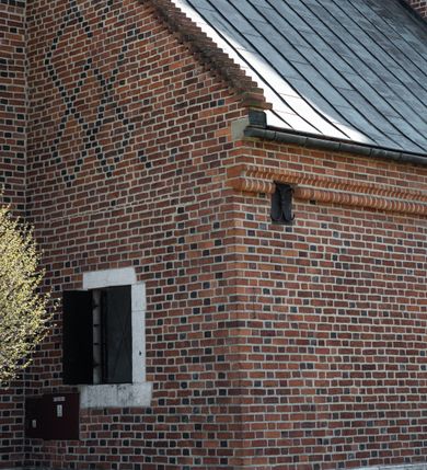 Zdjęcie nr 90: Kościół murowany z cegły, z użyciem zendrówki, na wysokim podmurowaniu z kamienia łupanego, jednonawowy, orientowany. 
Prezbiterium i nawa na planie prostokątów, nawa szersza i dłuższa od prezbiterium. Zakrystia na rzucie wydłużonego prostokąta przylega do wschodniej ściany prezbiterium, występując poza mury nawy. Prezbiterium od wschodu ujęte w narożach dwiema ukośnymi szkarpami, od południa jedną prostopadłą. Przy południowej ścianie nawy kruchta na planie kwadratu. Nawa w narożach ujęta szkarpami, od wschodu dwiema prostopadłymi, od zachodu ukośnymi. 
Prezbiterium dwuprzęsłowe, nakryte sklepieniem krzyżowo-żebrowym. Na zwornikach dwie tarcze z herbami Trzy Korony i Wieniawa. Zakrystia sklepiona kolebkowo. Nawa nakryta drewnianym stropem z kasetonami i rozetami. Kruchta sklepiona krzyżowo-żebrowo ze zwornikiem z tarczą z herbem Wieniawa. Otwór tęczowy w formie stojącego prostokąta zamkniętego łukiem ostrym. W zachodniej części nawy drewniany parapet chóru muzycznego wsparty na dwóch filarach. 
Fasada w jednej trzeciej wysokości odcięta kamiennym gzymsem kapnikowym, zakończona jodełkowym fryzem w partii muru, zwieńczona trójkątnym szczytem. Mur dekorowany zendrówką ułożoną „w zęby”, w partii szczytu w układzie rombowym. Na osi kamienny ostrołukowy portal o schodkowym nadprożu, dekorowanym krzyżującym się laskowaniem; węgary gładkie w jednej trzeciej wysokości przechodzące w piramidki i profilowanie powyżej. Nad portalem kamienna kwadratowa tablica, ujęta kamiennym obramieniem z tarczą z herbem Wieniawa. Ponad nią, na osi okulus w kamiennym obramieniu. 
Elewacje północna i południowa w części nawy w jednej trzeciej wysokości przedzielone kamiennym gzymsem kapnikowym, na zakończeniu ścian z gzymsem wieńczącym. Mur dekorowany zendrówką w układzie rombowym. Na elewacji południowej cztery okna w formie wydłużonego, stojącego prostokąta zamkniętego łukiem ostrym, w kamiennych obramieniach, podzielone laskowaniem. Południowa ściana prezbiterium zakończona gzymsem wieńczącym, w górnej części muru dekorowana zendrówką ułożoną „w zęby”. 
Szkarpy opinające nawę uskokowe, zwężające się ku górze, nakryte daszkami pulpitowymi. Szkarpy opinające prezbiterium nakryte daszkami pulpitowymi, podzielone gzymsami kapnikowymi. 
Kruchta od strony wschodniej i zachodniej podzielona kamiennym gzymsem kapnikowym, od południa zakończona gzymsem wieńczącym. Na ścianie południowej kruchty kamienny, ostrołukowy portal, o schodkowym nadprożu, dekorowanym krzyżującym się laskowaniem; węgary gładkie, w jednej trzeciej wysokości przechodzące w piramidki i profilowanie powyżej. Nad portalem kamienna tarcza z herbem Wieniawa. 
Elewacja wschodnia zwieńczona trójkątnym szczytem, w którego partii mur dekorowany jest zendrówką w układzie rombowym. Na osi okno w formie wydłużonego, stojącego prostokąta zamkniętego łukiem ostrym, w kamiennym obramieniu, zamurowane w trzech piątych wysokości, zakończone daszkiem pulpitowym. W dolnej części okna znajduje się ogrójec. 
Nawa i prezbiterium nakryte osobnymi blaszanymi dachami dwuspadowymi, kruchta i zakrystia pulpitowymi. Nad nawą blaszana wieżyczka na sygnaturkę z latarnią i hełmem baniastym.





