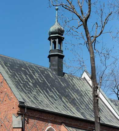 Zdjęcie nr 97: Kościół murowany z cegły, z użyciem zendrówki, na wysokim podmurowaniu z kamienia łupanego, jednonawowy, orientowany. 
Prezbiterium i nawa na planie prostokątów, nawa szersza i dłuższa od prezbiterium. Zakrystia na rzucie wydłużonego prostokąta przylega do wschodniej ściany prezbiterium, występując poza mury nawy. Prezbiterium od wschodu ujęte w narożach dwiema ukośnymi szkarpami, od południa jedną prostopadłą. Przy południowej ścianie nawy kruchta na planie kwadratu. Nawa w narożach ujęta szkarpami, od wschodu dwiema prostopadłymi, od zachodu ukośnymi. 
Prezbiterium dwuprzęsłowe, nakryte sklepieniem krzyżowo-żebrowym. Na zwornikach dwie tarcze z herbami Trzy Korony i Wieniawa. Zakrystia sklepiona kolebkowo. Nawa nakryta drewnianym stropem z kasetonami i rozetami. Kruchta sklepiona krzyżowo-żebrowo ze zwornikiem z tarczą z herbem Wieniawa. Otwór tęczowy w formie stojącego prostokąta zamkniętego łukiem ostrym. W zachodniej części nawy drewniany parapet chóru muzycznego wsparty na dwóch filarach. 
Fasada w jednej trzeciej wysokości odcięta kamiennym gzymsem kapnikowym, zakończona jodełkowym fryzem w partii muru, zwieńczona trójkątnym szczytem. Mur dekorowany zendrówką ułożoną „w zęby”, w partii szczytu w układzie rombowym. Na osi kamienny ostrołukowy portal o schodkowym nadprożu, dekorowanym krzyżującym się laskowaniem; węgary gładkie w jednej trzeciej wysokości przechodzące w piramidki i profilowanie powyżej. Nad portalem kamienna kwadratowa tablica, ujęta kamiennym obramieniem z tarczą z herbem Wieniawa. Ponad nią, na osi okulus w kamiennym obramieniu. 
Elewacje północna i południowa w części nawy w jednej trzeciej wysokości przedzielone kamiennym gzymsem kapnikowym, na zakończeniu ścian z gzymsem wieńczącym. Mur dekorowany zendrówką w układzie rombowym. Na elewacji południowej cztery okna w formie wydłużonego, stojącego prostokąta zamkniętego łukiem ostrym, w kamiennych obramieniach, podzielone laskowaniem. Południowa ściana prezbiterium zakończona gzymsem wieńczącym, w górnej części muru dekorowana zendrówką ułożoną „w zęby”. 
Szkarpy opinające nawę uskokowe, zwężające się ku górze, nakryte daszkami pulpitowymi. Szkarpy opinające prezbiterium nakryte daszkami pulpitowymi, podzielone gzymsami kapnikowymi. 
Kruchta od strony wschodniej i zachodniej podzielona kamiennym gzymsem kapnikowym, od południa zakończona gzymsem wieńczącym. Na ścianie południowej kruchty kamienny, ostrołukowy portal, o schodkowym nadprożu, dekorowanym krzyżującym się laskowaniem; węgary gładkie, w jednej trzeciej wysokości przechodzące w piramidki i profilowanie powyżej. Nad portalem kamienna tarcza z herbem Wieniawa. 
Elewacja wschodnia zwieńczona trójkątnym szczytem, w którego partii mur dekorowany jest zendrówką w układzie rombowym. Na osi okno w formie wydłużonego, stojącego prostokąta zamkniętego łukiem ostrym, w kamiennym obramieniu, zamurowane w trzech piątych wysokości, zakończone daszkiem pulpitowym. W dolnej części okna znajduje się ogrójec. 
Nawa i prezbiterium nakryte osobnymi blaszanymi dachami dwuspadowymi, kruchta i zakrystia pulpitowymi. Nad nawą blaszana wieżyczka na sygnaturkę z latarnią i hełmem baniastym.





