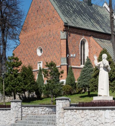 Zdjęcie nr 92: Kościół murowany z cegły, z użyciem zendrówki, na wysokim podmurowaniu z kamienia łupanego, jednonawowy, orientowany. 
Prezbiterium i nawa na planie prostokątów, nawa szersza i dłuższa od prezbiterium. Zakrystia na rzucie wydłużonego prostokąta przylega do wschodniej ściany prezbiterium, występując poza mury nawy. Prezbiterium od wschodu ujęte w narożach dwiema ukośnymi szkarpami, od południa jedną prostopadłą. Przy południowej ścianie nawy kruchta na planie kwadratu. Nawa w narożach ujęta szkarpami, od wschodu dwiema prostopadłymi, od zachodu ukośnymi. 
Prezbiterium dwuprzęsłowe, nakryte sklepieniem krzyżowo-żebrowym. Na zwornikach dwie tarcze z herbami Trzy Korony i Wieniawa. Zakrystia sklepiona kolebkowo. Nawa nakryta drewnianym stropem z kasetonami i rozetami. Kruchta sklepiona krzyżowo-żebrowo ze zwornikiem z tarczą z herbem Wieniawa. Otwór tęczowy w formie stojącego prostokąta zamkniętego łukiem ostrym. W zachodniej części nawy drewniany parapet chóru muzycznego wsparty na dwóch filarach. 
Fasada w jednej trzeciej wysokości odcięta kamiennym gzymsem kapnikowym, zakończona jodełkowym fryzem w partii muru, zwieńczona trójkątnym szczytem. Mur dekorowany zendrówką ułożoną „w zęby”, w partii szczytu w układzie rombowym. Na osi kamienny ostrołukowy portal o schodkowym nadprożu, dekorowanym krzyżującym się laskowaniem; węgary gładkie w jednej trzeciej wysokości przechodzące w piramidki i profilowanie powyżej. Nad portalem kamienna kwadratowa tablica, ujęta kamiennym obramieniem z tarczą z herbem Wieniawa. Ponad nią, na osi okulus w kamiennym obramieniu. 
Elewacje północna i południowa w części nawy w jednej trzeciej wysokości przedzielone kamiennym gzymsem kapnikowym, na zakończeniu ścian z gzymsem wieńczącym. Mur dekorowany zendrówką w układzie rombowym. Na elewacji południowej cztery okna w formie wydłużonego, stojącego prostokąta zamkniętego łukiem ostrym, w kamiennych obramieniach, podzielone laskowaniem. Południowa ściana prezbiterium zakończona gzymsem wieńczącym, w górnej części muru dekorowana zendrówką ułożoną „w zęby”. 
Szkarpy opinające nawę uskokowe, zwężające się ku górze, nakryte daszkami pulpitowymi. Szkarpy opinające prezbiterium nakryte daszkami pulpitowymi, podzielone gzymsami kapnikowymi. 
Kruchta od strony wschodniej i zachodniej podzielona kamiennym gzymsem kapnikowym, od południa zakończona gzymsem wieńczącym. Na ścianie południowej kruchty kamienny, ostrołukowy portal, o schodkowym nadprożu, dekorowanym krzyżującym się laskowaniem; węgary gładkie, w jednej trzeciej wysokości przechodzące w piramidki i profilowanie powyżej. Nad portalem kamienna tarcza z herbem Wieniawa. 
Elewacja wschodnia zwieńczona trójkątnym szczytem, w którego partii mur dekorowany jest zendrówką w układzie rombowym. Na osi okno w formie wydłużonego, stojącego prostokąta zamkniętego łukiem ostrym, w kamiennym obramieniu, zamurowane w trzech piątych wysokości, zakończone daszkiem pulpitowym. W dolnej części okna znajduje się ogrójec. 
Nawa i prezbiterium nakryte osobnymi blaszanymi dachami dwuspadowymi, kruchta i zakrystia pulpitowymi. Nad nawą blaszana wieżyczka na sygnaturkę z latarnią i hełmem baniastym.





