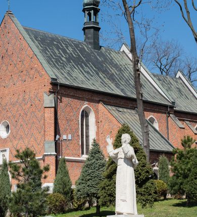 Zdjęcie nr 6: Kościół murowany z cegły, z użyciem zendrówki, na wysokim podmurowaniu z kamienia łupanego, jednonawowy, orientowany. 
Prezbiterium i nawa na planie prostokątów, nawa szersza i dłuższa od prezbiterium. Zakrystia na rzucie wydłużonego prostokąta przylega do wschodniej ściany prezbiterium, występując poza mury nawy. Prezbiterium od wschodu ujęte w narożach dwiema ukośnymi szkarpami, od południa jedną prostopadłą. Przy południowej ścianie nawy kruchta na planie kwadratu. Nawa w narożach ujęta szkarpami, od wschodu dwiema prostopadłymi, od zachodu ukośnymi. 
Prezbiterium dwuprzęsłowe, nakryte sklepieniem krzyżowo-żebrowym. Na zwornikach dwie tarcze z herbami Trzy Korony i Wieniawa. Zakrystia sklepiona kolebkowo. Nawa nakryta drewnianym stropem z kasetonami i rozetami. Kruchta sklepiona krzyżowo-żebrowo ze zwornikiem z tarczą z herbem Wieniawa. Otwór tęczowy w formie stojącego prostokąta zamkniętego łukiem ostrym. W zachodniej części nawy drewniany parapet chóru muzycznego wsparty na dwóch filarach. 
Fasada w jednej trzeciej wysokości odcięta kamiennym gzymsem kapnikowym, zakończona jodełkowym fryzem w partii muru, zwieńczona trójkątnym szczytem. Mur dekorowany zendrówką ułożoną „w zęby”, w partii szczytu w układzie rombowym. Na osi kamienny ostrołukowy portal o schodkowym nadprożu, dekorowanym krzyżującym się laskowaniem; węgary gładkie w jednej trzeciej wysokości przechodzące w piramidki i profilowanie powyżej. Nad portalem kamienna kwadratowa tablica, ujęta kamiennym obramieniem z tarczą z herbem Wieniawa. Ponad nią, na osi okulus w kamiennym obramieniu. 
Elewacje północna i południowa w części nawy w jednej trzeciej wysokości przedzielone kamiennym gzymsem kapnikowym, na zakończeniu ścian z gzymsem wieńczącym. Mur dekorowany zendrówką w układzie rombowym. Na elewacji południowej cztery okna w formie wydłużonego, stojącego prostokąta zamkniętego łukiem ostrym, w kamiennych obramieniach, podzielone laskowaniem. Południowa ściana prezbiterium zakończona gzymsem wieńczącym, w górnej części muru dekorowana zendrówką ułożoną „w zęby”. 
Szkarpy opinające nawę uskokowe, zwężające się ku górze, nakryte daszkami pulpitowymi. Szkarpy opinające prezbiterium nakryte daszkami pulpitowymi, podzielone gzymsami kapnikowymi. 
Kruchta od strony wschodniej i zachodniej podzielona kamiennym gzymsem kapnikowym, od południa zakończona gzymsem wieńczącym. Na ścianie południowej kruchty kamienny, ostrołukowy portal, o schodkowym nadprożu, dekorowanym krzyżującym się laskowaniem; węgary gładkie, w jednej trzeciej wysokości przechodzące w piramidki i profilowanie powyżej. Nad portalem kamienna tarcza z herbem Wieniawa. 
Elewacja wschodnia zwieńczona trójkątnym szczytem, w którego partii mur dekorowany jest zendrówką w układzie rombowym. Na osi okno w formie wydłużonego, stojącego prostokąta zamkniętego łukiem ostrym, w kamiennym obramieniu, zamurowane w trzech piątych wysokości, zakończone daszkiem pulpitowym. W dolnej części okna znajduje się ogrójec. 
Nawa i prezbiterium nakryte osobnymi blaszanymi dachami dwuspadowymi, kruchta i zakrystia pulpitowymi. Nad nawą blaszana wieżyczka na sygnaturkę z latarnią i hełmem baniastym.





