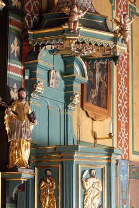 Zdjęcie nr 1: Ambona przyścienna, wisząca, z dostępem od zakrystii. Kosz na planie czterech boków z sześcioboku, na cokole w formie spłaszczonego wałka, z podwieszonym niewielkim cokolikiem zakończonym szyszką. Ścianki wydzielone pilastrami o kanelowanych trzonach, na cokołach, dźwigającymi parapet w formie gzymsu, wyłamany na ich osi. W polach ścianek płyciny o kształcie stojącego prostokąta z płaskorzeźbionymi przedstawieniami czterech ewangelistów. Zaplecek w formie wydłużonego, stojącego prostokąta, ujętego pilastrami o kanelowanych trzonach, zakończonych konsolami dekorowanymi liściem akantu, dźwigającymi imposty oraz przerwany, półokrągły przyczółek. W polu zaplecka drzwiczki do zakrystii, zdobione dwiema arkadami; ponad nimi płaskorzeźbione tablice praw. Baldachim na planie analogicznym względem kosza, w formie kopułki na wklęsłym, zwężającym się cokole dekorowanym płycinami, zakończonej latarnią z krzyżem na kuli. Brzeg w postaci gzymsu wyłamanego na osi podpór kosza, z siedzącymi nań puttami oraz z podwieszonym lambrekinem. Na podniebiu baldachimu rzeźbiona gołębica Ducha Świętego w glorii promienistej. 
Struktura polichromowana w kolorze szaro-niebieskim, profile i ornamentyka złocone.