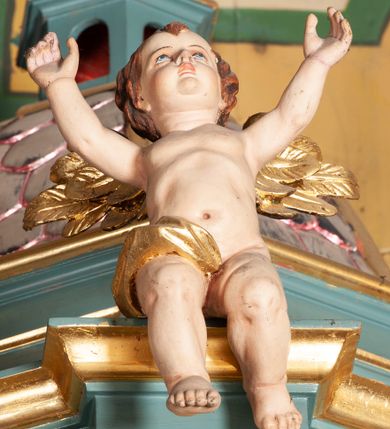 Zdjęcie nr 11: Ambona przyścienna, wisząca, z dostępem od zakrystii. Kosz na planie czterech boków z sześcioboku, na cokole w formie spłaszczonego wałka, z podwieszonym niewielkim cokolikiem zakończonym szyszką. Ścianki wydzielone pilastrami o kanelowanych trzonach, na cokołach, dźwigającymi parapet w formie gzymsu, wyłamany na ich osi. W polach ścianek płyciny o kształcie stojącego prostokąta z płaskorzeźbionymi przedstawieniami czterech ewangelistów. Zaplecek w formie wydłużonego, stojącego prostokąta, ujętego pilastrami o kanelowanych trzonach, zakończonych konsolami dekorowanymi liściem akantu, dźwigającymi imposty oraz przerwany, półokrągły przyczółek. W polu zaplecka drzwiczki do zakrystii, zdobione dwiema arkadami; ponad nimi płaskorzeźbione tablice praw. Baldachim na planie analogicznym względem kosza, w formie kopułki na wklęsłym, zwężającym się cokole dekorowanym płycinami, zakończonej latarnią z krzyżem na kuli. Brzeg w postaci gzymsu wyłamanego na osi podpór kosza, z siedzącymi nań puttami oraz z podwieszonym lambrekinem. Na podniebiu baldachimu rzeźbiona gołębica Ducha Świętego w glorii promienistej. 
Struktura polichromowana w kolorze szaro-niebieskim, profile i ornamentyka złocone.