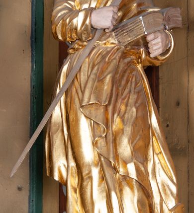 Zdjęcie nr 17: Ołtarz architektoniczny, jednokondygnacyjny, jednoosiowy, z bramkami i zwieńczeniem. Ołtarz kamienny, sarkofagowy, wklęsło-wypukły, na cokole. Mensa kamienna, o brzegu w formie profilowanego gzymsu. Tabernakulum drewniane, obite blachą, w postaci prostopadłościennej skrzynki, z wypukłą ścianką frontową, flankowane parą drewnianych kolumienek o kapitelach kompozytowych, na cokołach. Drzwiczki w formie kwadratu zamkniętego łukiem półkolistym, ujęte ramą z odlewaną dekoracją roślinną, w polu aplikowane, odlewane przedstawienie kielicha eucharystycznego w glorii promienistej na obłoku, z kłosami zbóż po bokach. Na tabernakulum osadzony tron wystawienia w formie prostopadłościanu, z wypukłą ścianką frontową oraz obrotową niszą ujętą profilowaną ramą, flankowany parą kolumienek o kapitelach kompozytowych, dźwigających imposty oraz przerwane w partii architrawu i fryzu belkowanie opasujące go z trzech stron. Na osi podpór przerwany, segmentowy przyczółek, ustawiony pod kątem. Na belkowaniu figurka Baranka Apokaliptycznego, leżącego na księdze na tle glorii promienistej. 
Retabulum na dwustrefowym cokole, w górnej partii zryzalitowanym przy brzegach, ujęte parą zwielokrotnionych pilastrów oraz stojącą przed nimi parą kolumn o kapitelach kompozytowych, ustawionych pod katem względem lica. Podpory dźwigają pełne belkowanie, wyłamane na ich osi, przerwane nad polem środkowym; na linii kolumn przerwany półokrągły przyczółek. W polu zwieńczenia gloria promienista z rzeźbioną gołębicą Ducha Świętego w otoczeniu obłoków i uskrzydlonych główek anielskich. W polu środkowym nisza w formie stojącego prostokąta zamkniętego łukiem segmentowym, w profilowanej ramie, z obrazem Matki Boskiej z Dzieciątkiem w aediculi. Bramki z przejściami w formie wydłużonego, stojącego prostokąta o wklęsłych górnych narożach, zamknięte dwoma spływami wolutowymi stanowiącymi podstawę dla cokołów na figury św. Piotra i św. Pawła. 
Cokoły kolumn dekorowane akantem. W polu środkowym, nad niszą para puttów podtrzymujących koronę; ramę flankują rocaillowe zwisy; u jej spodu palmety i rozety. Na brzegach belkowania wazony dekorowane plecionką i liśćmi. Kondygnacja ujęta uszami utworzonymi z wolut i liści palmowych. Spód cokołu wieńczącego bramki dekorowany muszlą; woluty zdobione kampanulami.
 Struktura polichromowana w kolorze szaro-niebieskim; kolumny, ramy, gloria, profile i ornamentyka złocone; obłoki srebrzone.
