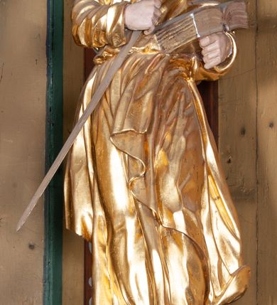 Zdjęcie nr 16: Ołtarz architektoniczny, jednokondygnacyjny, jednoosiowy, z bramkami i zwieńczeniem. Ołtarz kamienny, sarkofagowy, wklęsło-wypukły, na cokole. Mensa kamienna, o brzegu w formie profilowanego gzymsu. Tabernakulum drewniane, obite blachą, w postaci prostopadłościennej skrzynki, z wypukłą ścianką frontową, flankowane parą drewnianych kolumienek o kapitelach kompozytowych, na cokołach. Drzwiczki w formie kwadratu zamkniętego łukiem półkolistym, ujęte ramą z odlewaną dekoracją roślinną, w polu aplikowane, odlewane przedstawienie kielicha eucharystycznego w glorii promienistej na obłoku, z kłosami zbóż po bokach. Na tabernakulum osadzony tron wystawienia w formie prostopadłościanu, z wypukłą ścianką frontową oraz obrotową niszą ujętą profilowaną ramą, flankowany parą kolumienek o kapitelach kompozytowych, dźwigających imposty oraz przerwane w partii architrawu i fryzu belkowanie opasujące go z trzech stron. Na osi podpór przerwany, segmentowy przyczółek, ustawiony pod kątem. Na belkowaniu figurka Baranka Apokaliptycznego, leżącego na księdze na tle glorii promienistej. 
Retabulum na dwustrefowym cokole, w górnej partii zryzalitowanym przy brzegach, ujęte parą zwielokrotnionych pilastrów oraz stojącą przed nimi parą kolumn o kapitelach kompozytowych, ustawionych pod katem względem lica. Podpory dźwigają pełne belkowanie, wyłamane na ich osi, przerwane nad polem środkowym; na linii kolumn przerwany półokrągły przyczółek. W polu zwieńczenia gloria promienista z rzeźbioną gołębicą Ducha Świętego w otoczeniu obłoków i uskrzydlonych główek anielskich. W polu środkowym nisza w formie stojącego prostokąta zamkniętego łukiem segmentowym, w profilowanej ramie, z obrazem Matki Boskiej z Dzieciątkiem w aediculi. Bramki z przejściami w formie wydłużonego, stojącego prostokąta o wklęsłych górnych narożach, zamknięte dwoma spływami wolutowymi stanowiącymi podstawę dla cokołów na figury św. Piotra i św. Pawła. 
Cokoły kolumn dekorowane akantem. W polu środkowym, nad niszą para puttów podtrzymujących koronę; ramę flankują rocaillowe zwisy; u jej spodu palmety i rozety. Na brzegach belkowania wazony dekorowane plecionką i liśćmi. Kondygnacja ujęta uszami utworzonymi z wolut i liści palmowych. Spód cokołu wieńczącego bramki dekorowany muszlą; woluty zdobione kampanulami.
 Struktura polichromowana w kolorze szaro-niebieskim; kolumny, ramy, gloria, profile i ornamentyka złocone; obłoki srebrzone.
