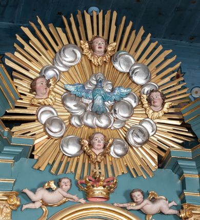 Zdjęcie nr 5: Ołtarz architektoniczny, jednokondygnacyjny, jednoosiowy, z bramkami i zwieńczeniem. Ołtarz kamienny, sarkofagowy, wklęsło-wypukły, na cokole. Mensa kamienna, o brzegu w formie profilowanego gzymsu. Tabernakulum drewniane, obite blachą, w postaci prostopadłościennej skrzynki, z wypukłą ścianką frontową, flankowane parą drewnianych kolumienek o kapitelach kompozytowych, na cokołach. Drzwiczki w formie kwadratu zamkniętego łukiem półkolistym, ujęte ramą z odlewaną dekoracją roślinną, w polu aplikowane, odlewane przedstawienie kielicha eucharystycznego w glorii promienistej na obłoku, z kłosami zbóż po bokach. Na tabernakulum osadzony tron wystawienia w formie prostopadłościanu, z wypukłą ścianką frontową oraz obrotową niszą ujętą profilowaną ramą, flankowany parą kolumienek o kapitelach kompozytowych, dźwigających imposty oraz przerwane w partii architrawu i fryzu belkowanie opasujące go z trzech stron. Na osi podpór przerwany, segmentowy przyczółek, ustawiony pod kątem. Na belkowaniu figurka Baranka Apokaliptycznego, leżącego na księdze na tle glorii promienistej. 
Retabulum na dwustrefowym cokole, w górnej partii zryzalitowanym przy brzegach, ujęte parą zwielokrotnionych pilastrów oraz stojącą przed nimi parą kolumn o kapitelach kompozytowych, ustawionych pod katem względem lica. Podpory dźwigają pełne belkowanie, wyłamane na ich osi, przerwane nad polem środkowym; na linii kolumn przerwany półokrągły przyczółek. W polu zwieńczenia gloria promienista z rzeźbioną gołębicą Ducha Świętego w otoczeniu obłoków i uskrzydlonych główek anielskich. W polu środkowym nisza w formie stojącego prostokąta zamkniętego łukiem segmentowym, w profilowanej ramie, z obrazem Matki Boskiej z Dzieciątkiem w aediculi. Bramki z przejściami w formie wydłużonego, stojącego prostokąta o wklęsłych górnych narożach, zamknięte dwoma spływami wolutowymi stanowiącymi podstawę dla cokołów na figury św. Piotra i św. Pawła. 
Cokoły kolumn dekorowane akantem. W polu środkowym, nad niszą para puttów podtrzymujących koronę; ramę flankują rocaillowe zwisy; u jej spodu palmety i rozety. Na brzegach belkowania wazony dekorowane plecionką i liśćmi. Kondygnacja ujęta uszami utworzonymi z wolut i liści palmowych. Spód cokołu wieńczącego bramki dekorowany muszlą; woluty zdobione kampanulami.
 Struktura polichromowana w kolorze szaro-niebieskim; kolumny, ramy, gloria, profile i ornamentyka złocone; obłoki srebrzone.

