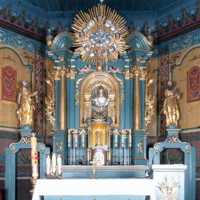 Zdjęcie nr 1: Ołtarz architektoniczny, jednokondygnacyjny, jednoosiowy, z bramkami i zwieńczeniem. Ołtarz kamienny, sarkofagowy, wklęsło-wypukły, na cokole. Mensa kamienna, o brzegu w formie profilowanego gzymsu. Tabernakulum drewniane, obite blachą, w postaci prostopadłościennej skrzynki, z wypukłą ścianką frontową, flankowane parą drewnianych kolumienek o kapitelach kompozytowych, na cokołach. Drzwiczki w formie kwadratu zamkniętego łukiem półkolistym, ujęte ramą z odlewaną dekoracją roślinną, w polu aplikowane, odlewane przedstawienie kielicha eucharystycznego w glorii promienistej na obłoku, z kłosami zbóż po bokach. Na tabernakulum osadzony tron wystawienia w formie prostopadłościanu, z wypukłą ścianką frontową oraz obrotową niszą ujętą profilowaną ramą, flankowany parą kolumienek o kapitelach kompozytowych, dźwigających imposty oraz przerwane w partii architrawu i fryzu belkowanie opasujące go z trzech stron. Na osi podpór przerwany, segmentowy przyczółek, ustawiony pod kątem. Na belkowaniu figurka Baranka Apokaliptycznego, leżącego na księdze na tle glorii promienistej. 
Retabulum na dwustrefowym cokole, w górnej partii zryzalitowanym przy brzegach, ujęte parą zwielokrotnionych pilastrów oraz stojącą przed nimi parą kolumn o kapitelach kompozytowych, ustawionych pod katem względem lica. Podpory dźwigają pełne belkowanie, wyłamane na ich osi, przerwane nad polem środkowym; na linii kolumn przerwany półokrągły przyczółek. W polu zwieńczenia gloria promienista z rzeźbioną gołębicą Ducha Świętego w otoczeniu obłoków i uskrzydlonych główek anielskich. W polu środkowym nisza w formie stojącego prostokąta zamkniętego łukiem segmentowym, w profilowanej ramie, z obrazem Matki Boskiej z Dzieciątkiem w aediculi. Bramki z przejściami w formie wydłużonego, stojącego prostokąta o wklęsłych górnych narożach, zamknięte dwoma spływami wolutowymi stanowiącymi podstawę dla cokołów na figury św. Piotra i św. Pawła. 
Cokoły kolumn dekorowane akantem. W polu środkowym, nad niszą para puttów podtrzymujących koronę; ramę flankują rocaillowe zwisy; u jej spodu palmety i rozety. Na brzegach belkowania wazony dekorowane plecionką i liśćmi. Kondygnacja ujęta uszami utworzonymi z wolut i liści palmowych. Spód cokołu wieńczącego bramki dekorowany muszlą; woluty zdobione kampanulami.
 Struktura polichromowana w kolorze szaro-niebieskim; kolumny, ramy, gloria, profile i ornamentyka złocone; obłoki srebrzone.
