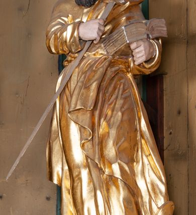 Zdjęcie nr 20: Ołtarz architektoniczny, jednokondygnacyjny, jednoosiowy, z bramkami i zwieńczeniem. Ołtarz kamienny, sarkofagowy, wklęsło-wypukły, na cokole. Mensa kamienna, o brzegu w formie profilowanego gzymsu. Tabernakulum drewniane, obite blachą, w postaci prostopadłościennej skrzynki, z wypukłą ścianką frontową, flankowane parą drewnianych kolumienek o kapitelach kompozytowych, na cokołach. Drzwiczki w formie kwadratu zamkniętego łukiem półkolistym, ujęte ramą z odlewaną dekoracją roślinną, w polu aplikowane, odlewane przedstawienie kielicha eucharystycznego w glorii promienistej na obłoku, z kłosami zbóż po bokach. Na tabernakulum osadzony tron wystawienia w formie prostopadłościanu, z wypukłą ścianką frontową oraz obrotową niszą ujętą profilowaną ramą, flankowany parą kolumienek o kapitelach kompozytowych, dźwigających imposty oraz przerwane w partii architrawu i fryzu belkowanie opasujące go z trzech stron. Na osi podpór przerwany, segmentowy przyczółek, ustawiony pod kątem. Na belkowaniu figurka Baranka Apokaliptycznego, leżącego na księdze na tle glorii promienistej. 
Retabulum na dwustrefowym cokole, w górnej partii zryzalitowanym przy brzegach, ujęte parą zwielokrotnionych pilastrów oraz stojącą przed nimi parą kolumn o kapitelach kompozytowych, ustawionych pod katem względem lica. Podpory dźwigają pełne belkowanie, wyłamane na ich osi, przerwane nad polem środkowym; na linii kolumn przerwany półokrągły przyczółek. W polu zwieńczenia gloria promienista z rzeźbioną gołębicą Ducha Świętego w otoczeniu obłoków i uskrzydlonych główek anielskich. W polu środkowym nisza w formie stojącego prostokąta zamkniętego łukiem segmentowym, w profilowanej ramie, z obrazem Matki Boskiej z Dzieciątkiem w aediculi. Bramki z przejściami w formie wydłużonego, stojącego prostokąta o wklęsłych górnych narożach, zamknięte dwoma spływami wolutowymi stanowiącymi podstawę dla cokołów na figury św. Piotra i św. Pawła. 
Cokoły kolumn dekorowane akantem. W polu środkowym, nad niszą para puttów podtrzymujących koronę; ramę flankują rocaillowe zwisy; u jej spodu palmety i rozety. Na brzegach belkowania wazony dekorowane plecionką i liśćmi. Kondygnacja ujęta uszami utworzonymi z wolut i liści palmowych. Spód cokołu wieńczącego bramki dekorowany muszlą; woluty zdobione kampanulami.
 Struktura polichromowana w kolorze szaro-niebieskim; kolumny, ramy, gloria, profile i ornamentyka złocone; obłoki srebrzone.
