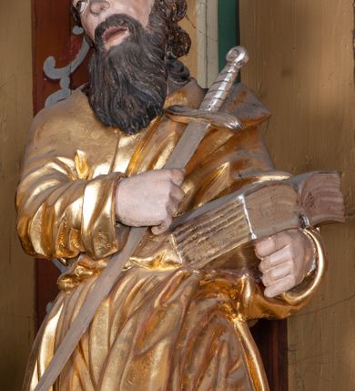 Zdjęcie nr 22: Ołtarz architektoniczny, jednokondygnacyjny, jednoosiowy, z bramkami i zwieńczeniem. Ołtarz kamienny, sarkofagowy, wklęsło-wypukły, na cokole. Mensa kamienna, o brzegu w formie profilowanego gzymsu. Tabernakulum drewniane, obite blachą, w postaci prostopadłościennej skrzynki, z wypukłą ścianką frontową, flankowane parą drewnianych kolumienek o kapitelach kompozytowych, na cokołach. Drzwiczki w formie kwadratu zamkniętego łukiem półkolistym, ujęte ramą z odlewaną dekoracją roślinną, w polu aplikowane, odlewane przedstawienie kielicha eucharystycznego w glorii promienistej na obłoku, z kłosami zbóż po bokach. Na tabernakulum osadzony tron wystawienia w formie prostopadłościanu, z wypukłą ścianką frontową oraz obrotową niszą ujętą profilowaną ramą, flankowany parą kolumienek o kapitelach kompozytowych, dźwigających imposty oraz przerwane w partii architrawu i fryzu belkowanie opasujące go z trzech stron. Na osi podpór przerwany, segmentowy przyczółek, ustawiony pod kątem. Na belkowaniu figurka Baranka Apokaliptycznego, leżącego na księdze na tle glorii promienistej. 
Retabulum na dwustrefowym cokole, w górnej partii zryzalitowanym przy brzegach, ujęte parą zwielokrotnionych pilastrów oraz stojącą przed nimi parą kolumn o kapitelach kompozytowych, ustawionych pod katem względem lica. Podpory dźwigają pełne belkowanie, wyłamane na ich osi, przerwane nad polem środkowym; na linii kolumn przerwany półokrągły przyczółek. W polu zwieńczenia gloria promienista z rzeźbioną gołębicą Ducha Świętego w otoczeniu obłoków i uskrzydlonych główek anielskich. W polu środkowym nisza w formie stojącego prostokąta zamkniętego łukiem segmentowym, w profilowanej ramie, z obrazem Matki Boskiej z Dzieciątkiem w aediculi. Bramki z przejściami w formie wydłużonego, stojącego prostokąta o wklęsłych górnych narożach, zamknięte dwoma spływami wolutowymi stanowiącymi podstawę dla cokołów na figury św. Piotra i św. Pawła. 
Cokoły kolumn dekorowane akantem. W polu środkowym, nad niszą para puttów podtrzymujących koronę; ramę flankują rocaillowe zwisy; u jej spodu palmety i rozety. Na brzegach belkowania wazony dekorowane plecionką i liśćmi. Kondygnacja ujęta uszami utworzonymi z wolut i liści palmowych. Spód cokołu wieńczącego bramki dekorowany muszlą; woluty zdobione kampanulami.
 Struktura polichromowana w kolorze szaro-niebieskim; kolumny, ramy, gloria, profile i ornamentyka złocone; obłoki srebrzone.
