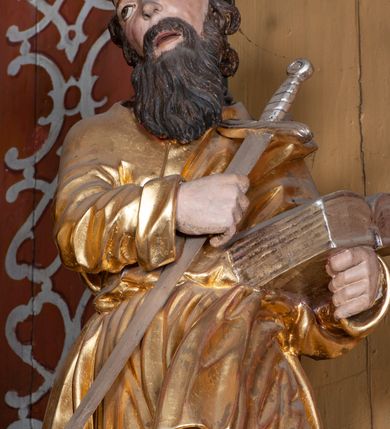 Zdjęcie nr 19: Ołtarz architektoniczny, jednokondygnacyjny, jednoosiowy, z bramkami i zwieńczeniem. Ołtarz kamienny, sarkofagowy, wklęsło-wypukły, na cokole. Mensa kamienna, o brzegu w formie profilowanego gzymsu. Tabernakulum drewniane, obite blachą, w postaci prostopadłościennej skrzynki, z wypukłą ścianką frontową, flankowane parą drewnianych kolumienek o kapitelach kompozytowych, na cokołach. Drzwiczki w formie kwadratu zamkniętego łukiem półkolistym, ujęte ramą z odlewaną dekoracją roślinną, w polu aplikowane, odlewane przedstawienie kielicha eucharystycznego w glorii promienistej na obłoku, z kłosami zbóż po bokach. Na tabernakulum osadzony tron wystawienia w formie prostopadłościanu, z wypukłą ścianką frontową oraz obrotową niszą ujętą profilowaną ramą, flankowany parą kolumienek o kapitelach kompozytowych, dźwigających imposty oraz przerwane w partii architrawu i fryzu belkowanie opasujące go z trzech stron. Na osi podpór przerwany, segmentowy przyczółek, ustawiony pod kątem. Na belkowaniu figurka Baranka Apokaliptycznego, leżącego na księdze na tle glorii promienistej. 
Retabulum na dwustrefowym cokole, w górnej partii zryzalitowanym przy brzegach, ujęte parą zwielokrotnionych pilastrów oraz stojącą przed nimi parą kolumn o kapitelach kompozytowych, ustawionych pod katem względem lica. Podpory dźwigają pełne belkowanie, wyłamane na ich osi, przerwane nad polem środkowym; na linii kolumn przerwany półokrągły przyczółek. W polu zwieńczenia gloria promienista z rzeźbioną gołębicą Ducha Świętego w otoczeniu obłoków i uskrzydlonych główek anielskich. W polu środkowym nisza w formie stojącego prostokąta zamkniętego łukiem segmentowym, w profilowanej ramie, z obrazem Matki Boskiej z Dzieciątkiem w aediculi. Bramki z przejściami w formie wydłużonego, stojącego prostokąta o wklęsłych górnych narożach, zamknięte dwoma spływami wolutowymi stanowiącymi podstawę dla cokołów na figury św. Piotra i św. Pawła. 
Cokoły kolumn dekorowane akantem. W polu środkowym, nad niszą para puttów podtrzymujących koronę; ramę flankują rocaillowe zwisy; u jej spodu palmety i rozety. Na brzegach belkowania wazony dekorowane plecionką i liśćmi. Kondygnacja ujęta uszami utworzonymi z wolut i liści palmowych. Spód cokołu wieńczącego bramki dekorowany muszlą; woluty zdobione kampanulami.
 Struktura polichromowana w kolorze szaro-niebieskim; kolumny, ramy, gloria, profile i ornamentyka złocone; obłoki srebrzone.
