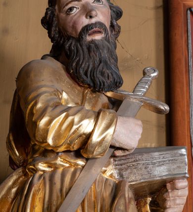 Zdjęcie nr 18: Ołtarz architektoniczny, jednokondygnacyjny, jednoosiowy, z bramkami i zwieńczeniem. Ołtarz kamienny, sarkofagowy, wklęsło-wypukły, na cokole. Mensa kamienna, o brzegu w formie profilowanego gzymsu. Tabernakulum drewniane, obite blachą, w postaci prostopadłościennej skrzynki, z wypukłą ścianką frontową, flankowane parą drewnianych kolumienek o kapitelach kompozytowych, na cokołach. Drzwiczki w formie kwadratu zamkniętego łukiem półkolistym, ujęte ramą z odlewaną dekoracją roślinną, w polu aplikowane, odlewane przedstawienie kielicha eucharystycznego w glorii promienistej na obłoku, z kłosami zbóż po bokach. Na tabernakulum osadzony tron wystawienia w formie prostopadłościanu, z wypukłą ścianką frontową oraz obrotową niszą ujętą profilowaną ramą, flankowany parą kolumienek o kapitelach kompozytowych, dźwigających imposty oraz przerwane w partii architrawu i fryzu belkowanie opasujące go z trzech stron. Na osi podpór przerwany, segmentowy przyczółek, ustawiony pod kątem. Na belkowaniu figurka Baranka Apokaliptycznego, leżącego na księdze na tle glorii promienistej. 
Retabulum na dwustrefowym cokole, w górnej partii zryzalitowanym przy brzegach, ujęte parą zwielokrotnionych pilastrów oraz stojącą przed nimi parą kolumn o kapitelach kompozytowych, ustawionych pod katem względem lica. Podpory dźwigają pełne belkowanie, wyłamane na ich osi, przerwane nad polem środkowym; na linii kolumn przerwany półokrągły przyczółek. W polu zwieńczenia gloria promienista z rzeźbioną gołębicą Ducha Świętego w otoczeniu obłoków i uskrzydlonych główek anielskich. W polu środkowym nisza w formie stojącego prostokąta zamkniętego łukiem segmentowym, w profilowanej ramie, z obrazem Matki Boskiej z Dzieciątkiem w aediculi. Bramki z przejściami w formie wydłużonego, stojącego prostokąta o wklęsłych górnych narożach, zamknięte dwoma spływami wolutowymi stanowiącymi podstawę dla cokołów na figury św. Piotra i św. Pawła. 
Cokoły kolumn dekorowane akantem. W polu środkowym, nad niszą para puttów podtrzymujących koronę; ramę flankują rocaillowe zwisy; u jej spodu palmety i rozety. Na brzegach belkowania wazony dekorowane plecionką i liśćmi. Kondygnacja ujęta uszami utworzonymi z wolut i liści palmowych. Spód cokołu wieńczącego bramki dekorowany muszlą; woluty zdobione kampanulami.
 Struktura polichromowana w kolorze szaro-niebieskim; kolumny, ramy, gloria, profile i ornamentyka złocone; obłoki srebrzone.
