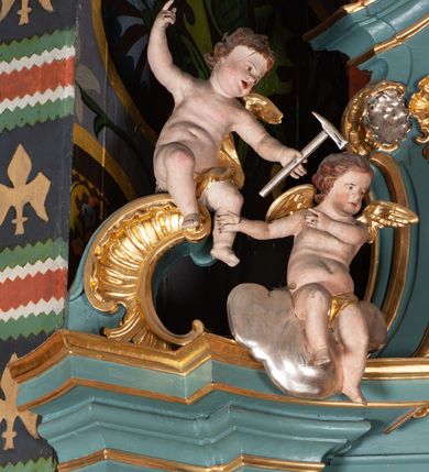 Zdjęcie nr 12: Ołtarz przyścienny, architektoniczny, jednoosiowy, jednokondygnacyjny ze zwieńczeniem. Mensa prostopadłościenna na niskim cokole. Nastawa ołtarzowa ustawiona na wysokim dwustrefowym cokole. Retabulum ujęte parą kolumn o stylizowanych, jońskich głowicach. Podpory wspierają belkowanie o wklęsłym wykroju, przerwane w części środkowej. Na gzymsie odcinki przyczółka o wolutowo skręconych końcach, skierowanych do wewnątrz. Zwieńczenie o wklęsłych bokach, zamknięte, dwoma stykającymi się wolutami z glorią promienistą. Pośrodku glorii symbol Opatrzności Bożej z IHS. Pole środkowe w formie prostokątnej wnęki ujętej ornamentem rocaille’owym. We wnęce rzeźbiony krucyfiks, zawieszony na tle malowanego pejzażu. Po bokach ołtarza, na osobnych konsolach ustawione figury Matki Boskiej po lewej oraz św. Jana Ewangelisty po prawej stronie. Po bokach zwieńczenia, na belkowaniu dwie pary rzeźbionych, uskrzydlonych aniołków. Boki wnęki środkowej dekorowane ornamentem rocaille’owym. Fontowe ścianki cokołów zdobione ażurowymi, wolutowo zwiniętymi liśćmi akantu. W zwieńczeniu obraz z przedstawieniem św. Michała Archanioła ujęty ramą formowaną z motywów „C” kształtnych. Struktura ołtarza malowana w kolorze niebieskim, boki mensy z prostokątnymi jasnobrązowymi płycinami, detal architektoniczny i profilowania złocone.

Figury uskrzydlonych aniołów pełnoplastyczne, ścięte z tyłu, siedzące na obłokach powyżej belkowania retabulum. Anioł po prawej stronie o szeroko rozłożonych rękach, głowie przechylonej w prawą stronę (h.). Anioł po lewej z rękoma uniesionymi, skierowanymi w prawo, głowa lekko pochylona, zwrócona w lewo. Figury niemal nagie, ze złotą przepaską wokół bioder. Twarze owalne o wydatnym czole okolone jasnobrązowymi włosami. Karnacja ciała w jasnokremowym odcieniu.