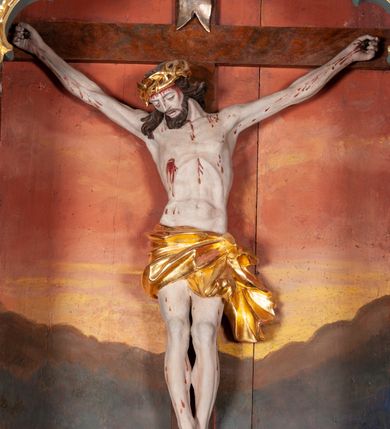 Zdjęcie nr 2: Figura Chrystusa ścięta z tyłu, przybita do belki krzyża trzema gwoździami, w typie Christo morte. Ciało w głębokim zwisie, ramiona ułożone w kształt litery „Y”. Głowa opadająca na klatkę piersiową, przechylona na prawe ramię. Twarz szeroka, okolona krótką brodą i włosami opadającymi na prawe ramię. Oczy zamknięte, nos niewielki, prosty, usta rozchylone. Na głowie korona cierniowa. Sylwetka ciała smukła o wyraźnie zaznaczonej muskulaturze, zwłaszcza w partii klatki piersiowej i ramion. Dłonie o zaciśniętych palcach. Wokół bioder perizonium układające się w głębokie poprzeczne fałdy, z rozwianym zwisem przy lewym boku. Stopy skrzyżowane, prawa założona na lewą. Karnacja ciała w jasnoszarym odcieniu z zaznaczonymi czerwoną farbą śladami męki. Włosy i zarost ciemnobrązowe, perizonium i korona cierniowa złote. Nad głową srebrny titulus w formie banderoli.