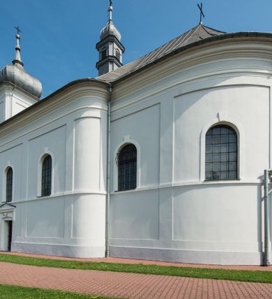 Zdjęcie nr 3: Murowany kościół otrzymał układ jednonawowej świątyni z węższym prezbiterium zwróconym ku północy i wieżą dostawioną do nawy od południa. Prezbiterium jest jednoprzęsłowe zakończone spłaszczoną apsydą. Na jego przedłużeniu usytuowano czworoboczną zakrystię. Prostokątna nawa jest trójprzęsłowa o zaokrąglonych narożnikach. Od frontu wzniesiono czworoboczną wieżę o ściętych narożnikach, flankowaną piętrowymi lokalnościami. Wysunięto ją lekko ku przodowi, gdzie przechodzi wklęsłymi płaszczyznami w boczne części fasady. Jej górne piętro nakryte cebulastym hełmem zostało opięte po bokach wolutami, obok których ustawiono kamienne klasycystyczne wazy. Elewacje zewnętrzne artykułowano podziałami ramowymi, zamykając wysokości ścian gzymsem gurtowy. Na końcu nawy na siodłowym dachu pokrytym blachą umieszczono czworoboczną wieżyczkę na sygnaturkę zwieńczoną cebulastym hełmem z krzyżem. Podobnym dachem nakryto prezbiterium. Wnętrze kościoła zostało rozczłonkowane lizenami z wklęsłymi półlizenami po bokach, ponad którymi rozciągnięto odcinki belkowania. Całość nakryto sklepieniem żaglastym na zdwojonych gurtach. Od południa w nawie urządzono chór muzyczny wsparty na dwóch kolumnach z parapetem wklęsłowypukłym. W prezbiterium usytuowano ołtarz główny, a w nawie dwa ołtarze boczne. Tu także na ścianie zachodniej zawieszono ambonę.  