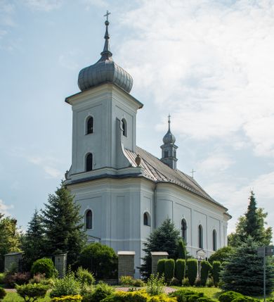 Zdjęcie nr 1: Murowany kościół otrzymał układ jednonawowej świątyni z węższym prezbiterium zwróconym ku północy i wieżą dostawioną do nawy od południa. Prezbiterium jest jednoprzęsłowe zakończone spłaszczoną apsydą. Na jego przedłużeniu usytuowano czworoboczną zakrystię. Prostokątna nawa jest trójprzęsłowa o zaokrąglonych narożnikach. Od frontu wzniesiono czworoboczną wieżę o ściętych narożnikach, flankowaną piętrowymi lokalnościami. Wysunięto ją lekko ku przodowi, gdzie przechodzi wklęsłymi płaszczyznami w boczne części fasady. Jej górne piętro nakryte cebulastym hełmem zostało opięte po bokach wolutami, obok których ustawiono kamienne klasycystyczne wazy. Elewacje zewnętrzne artykułowano podziałami ramowymi, zamykając wysokości ścian gzymsem gurtowy. Na końcu nawy na siodłowym dachu pokrytym blachą umieszczono czworoboczną wieżyczkę na sygnaturkę zwieńczoną cebulastym hełmem z krzyżem. Podobnym dachem nakryto prezbiterium. Wnętrze kościoła zostało rozczłonkowane lizenami z wklęsłymi półlizenami po bokach, ponad którymi rozciągnięto odcinki belkowania. Całość nakryto sklepieniem żaglastym na zdwojonych gurtach. Od południa w nawie urządzono chór muzyczny wsparty na dwóch kolumnach z parapetem wklęsłowypukłym. W prezbiterium usytuowano ołtarz główny, a w nawie dwa ołtarze boczne. Tu także na ścianie zachodniej zawieszono ambonę.  