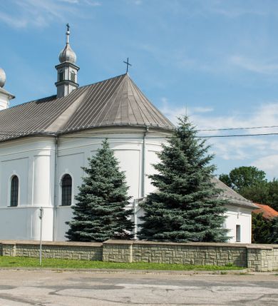 Zdjęcie nr 4: Murowany kościół otrzymał układ jednonawowej świątyni z węższym prezbiterium zwróconym ku północy i wieżą dostawioną do nawy od południa. Prezbiterium jest jednoprzęsłowe zakończone spłaszczoną apsydą. Na jego przedłużeniu usytuowano czworoboczną zakrystię. Prostokątna nawa jest trójprzęsłowa o zaokrąglonych narożnikach. Od frontu wzniesiono czworoboczną wieżę o ściętych narożnikach, flankowaną piętrowymi lokalnościami. Wysunięto ją lekko ku przodowi, gdzie przechodzi wklęsłymi płaszczyznami w boczne części fasady. Jej górne piętro nakryte cebulastym hełmem zostało opięte po bokach wolutami, obok których ustawiono kamienne klasycystyczne wazy. Elewacje zewnętrzne artykułowano podziałami ramowymi, zamykając wysokości ścian gzymsem gurtowy. Na końcu nawy na siodłowym dachu pokrytym blachą umieszczono czworoboczną wieżyczkę na sygnaturkę zwieńczoną cebulastym hełmem z krzyżem. Podobnym dachem nakryto prezbiterium. Wnętrze kościoła zostało rozczłonkowane lizenami z wklęsłymi półlizenami po bokach, ponad którymi rozciągnięto odcinki belkowania. Całość nakryto sklepieniem żaglastym na zdwojonych gurtach. Od południa w nawie urządzono chór muzyczny wsparty na dwóch kolumnach z parapetem wklęsłowypukłym. W prezbiterium usytuowano ołtarz główny, a w nawie dwa ołtarze boczne. Tu także na ścianie zachodniej zawieszono ambonę.  