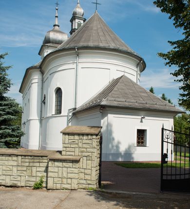 Zdjęcie nr 5: Murowany kościół otrzymał układ jednonawowej świątyni z węższym prezbiterium zwróconym ku północy i wieżą dostawioną do nawy od południa. Prezbiterium jest jednoprzęsłowe zakończone spłaszczoną apsydą. Na jego przedłużeniu usytuowano czworoboczną zakrystię. Prostokątna nawa jest trójprzęsłowa o zaokrąglonych narożnikach. Od frontu wzniesiono czworoboczną wieżę o ściętych narożnikach, flankowaną piętrowymi lokalnościami. Wysunięto ją lekko ku przodowi, gdzie przechodzi wklęsłymi płaszczyznami w boczne części fasady. Jej górne piętro nakryte cebulastym hełmem zostało opięte po bokach wolutami, obok których ustawiono kamienne klasycystyczne wazy. Elewacje zewnętrzne artykułowano podziałami ramowymi, zamykając wysokości ścian gzymsem gurtowy. Na końcu nawy na siodłowym dachu pokrytym blachą umieszczono czworoboczną wieżyczkę na sygnaturkę zwieńczoną cebulastym hełmem z krzyżem. Podobnym dachem nakryto prezbiterium. Wnętrze kościoła zostało rozczłonkowane lizenami z wklęsłymi półlizenami po bokach, ponad którymi rozciągnięto odcinki belkowania. Całość nakryto sklepieniem żaglastym na zdwojonych gurtach. Od południa w nawie urządzono chór muzyczny wsparty na dwóch kolumnach z parapetem wklęsłowypukłym. W prezbiterium usytuowano ołtarz główny, a w nawie dwa ołtarze boczne. Tu także na ścianie zachodniej zawieszono ambonę.  